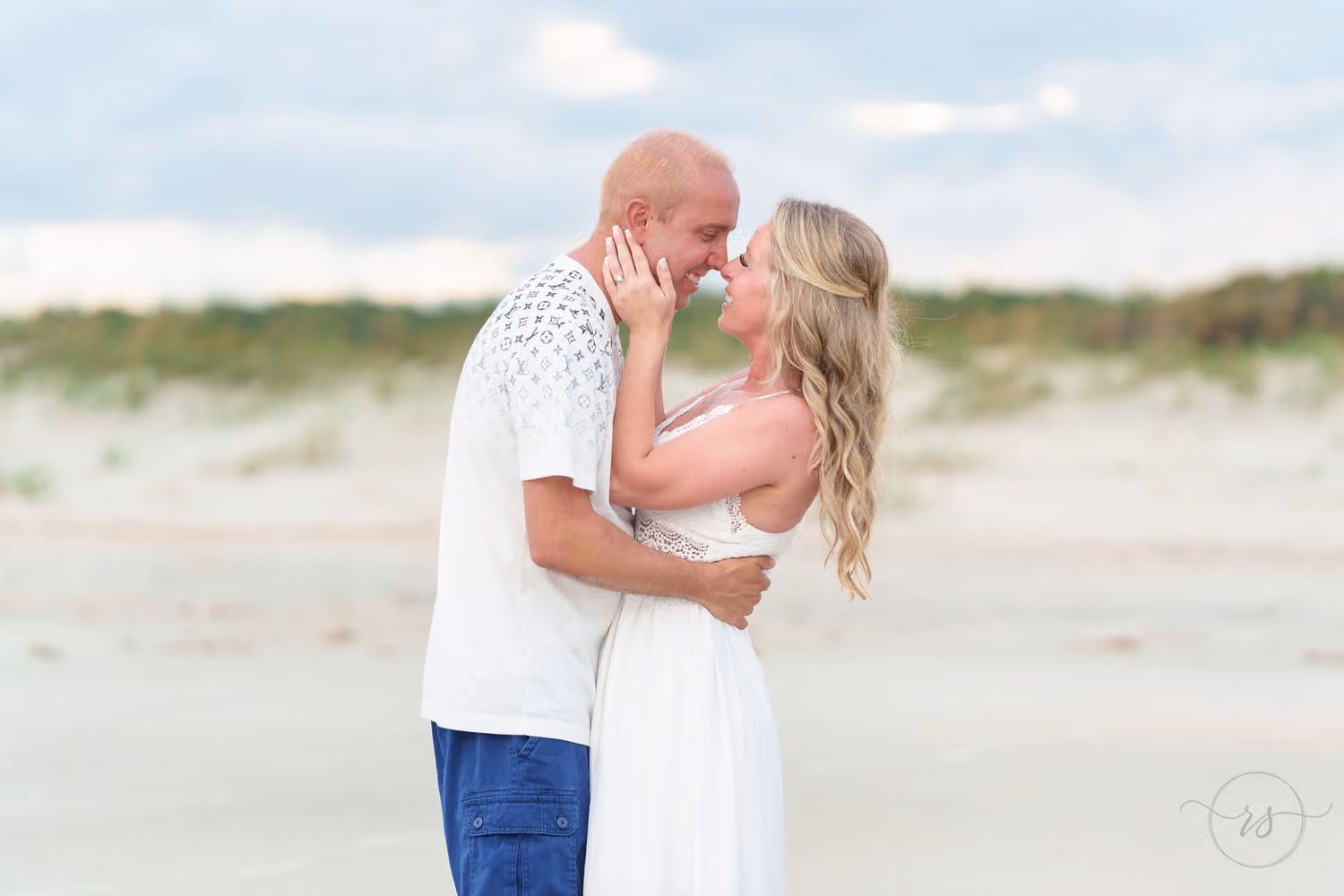 Couple touching noses in a close embrace on the beach with the dunes behind them at Huntington Beach State Park