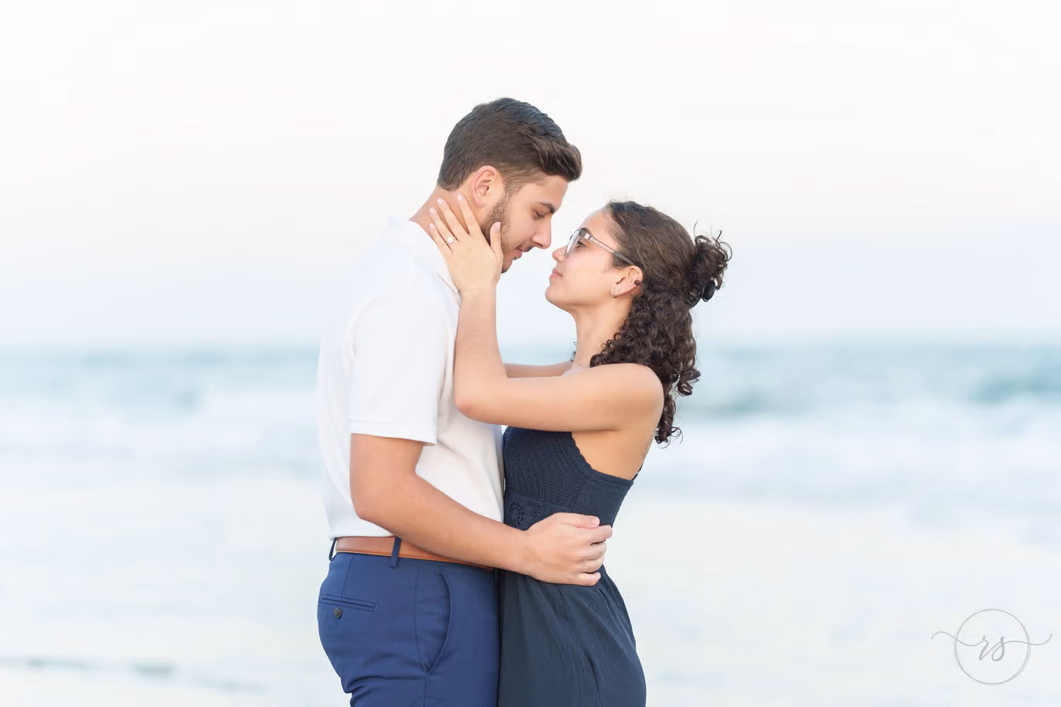Couple touching noses in a close embrace with the pale blue ocean behind them at Huntington Beach State Park