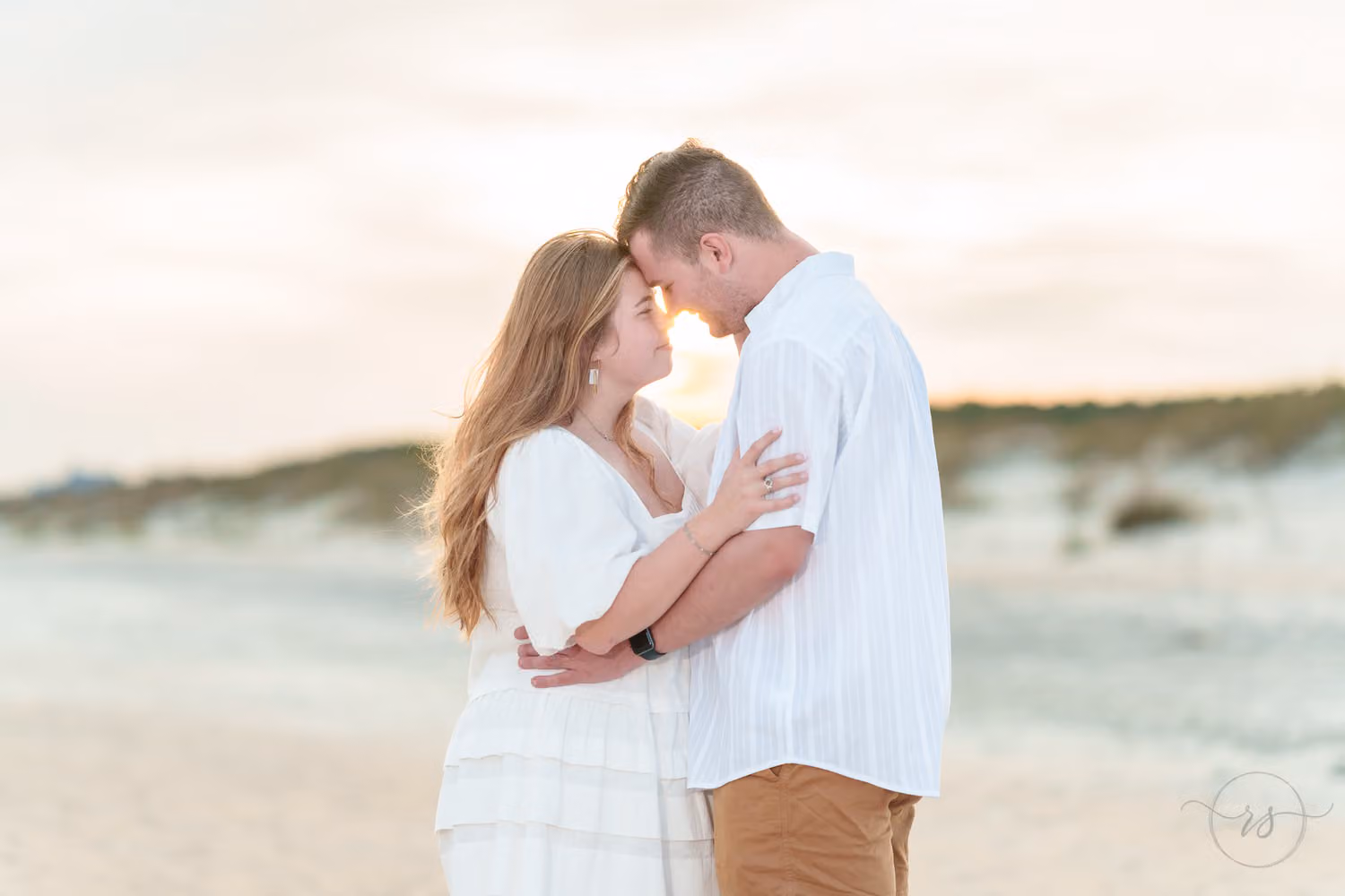 Couple touching noses in soft evening light with the dunes softly blurred behind at Huntington Beach State Park