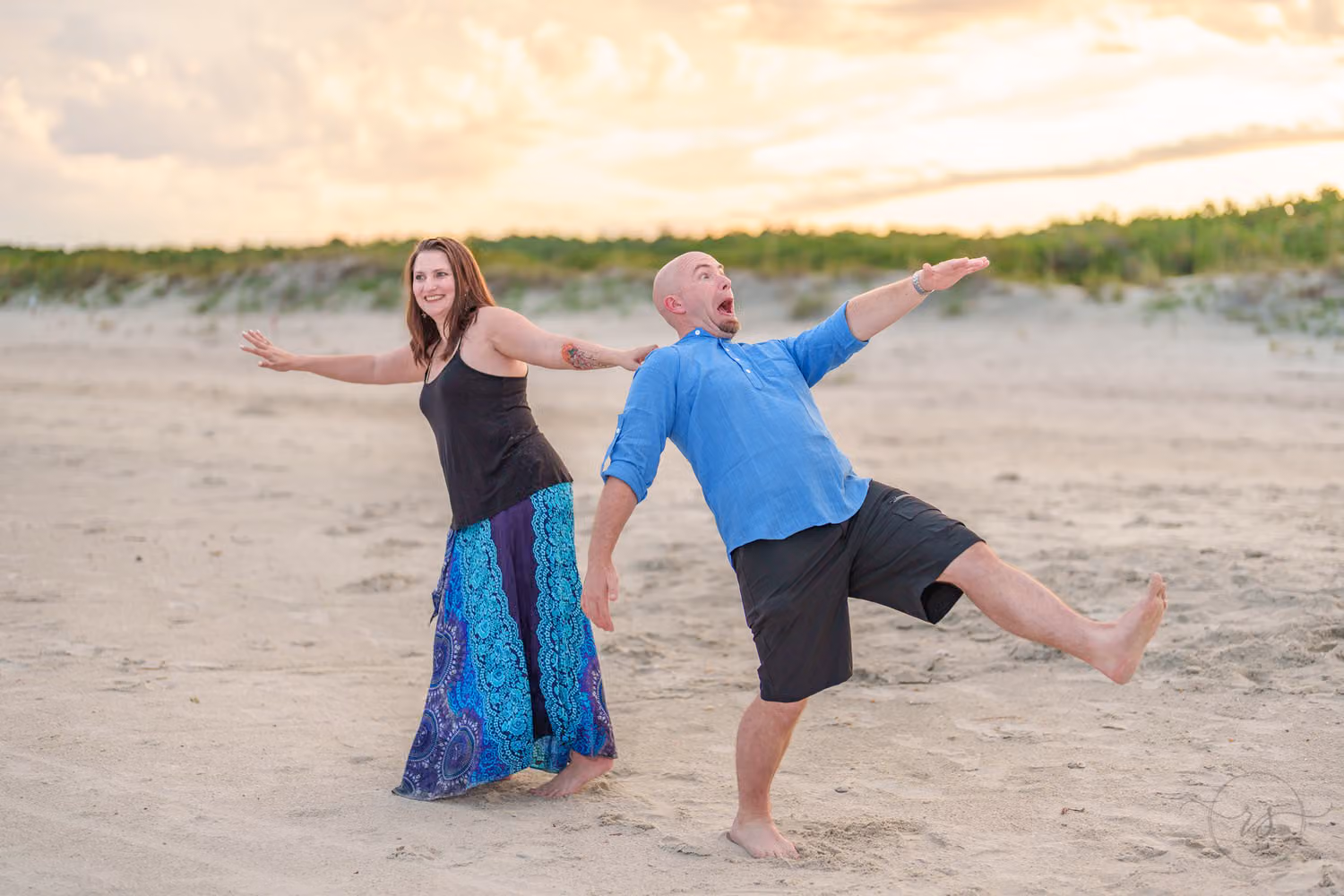 Laughing man kicking up a leg to run off as his fiancée reaches for him on the beach at Huntington Beach State Park