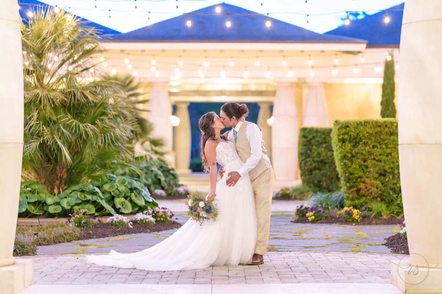 Groom leaning in to kiss the bride under string lights in the courtyard at twilight at 21 Main Events