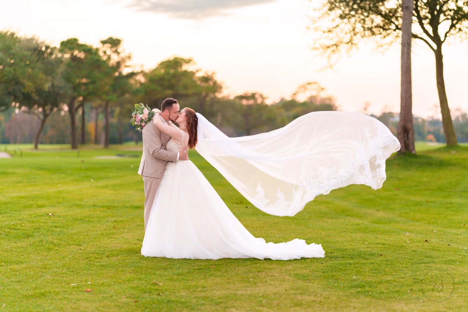 Bride's long veil blowing in the wind as the couple kisses on the golf course after sunset at Pine Lakes Country Club
