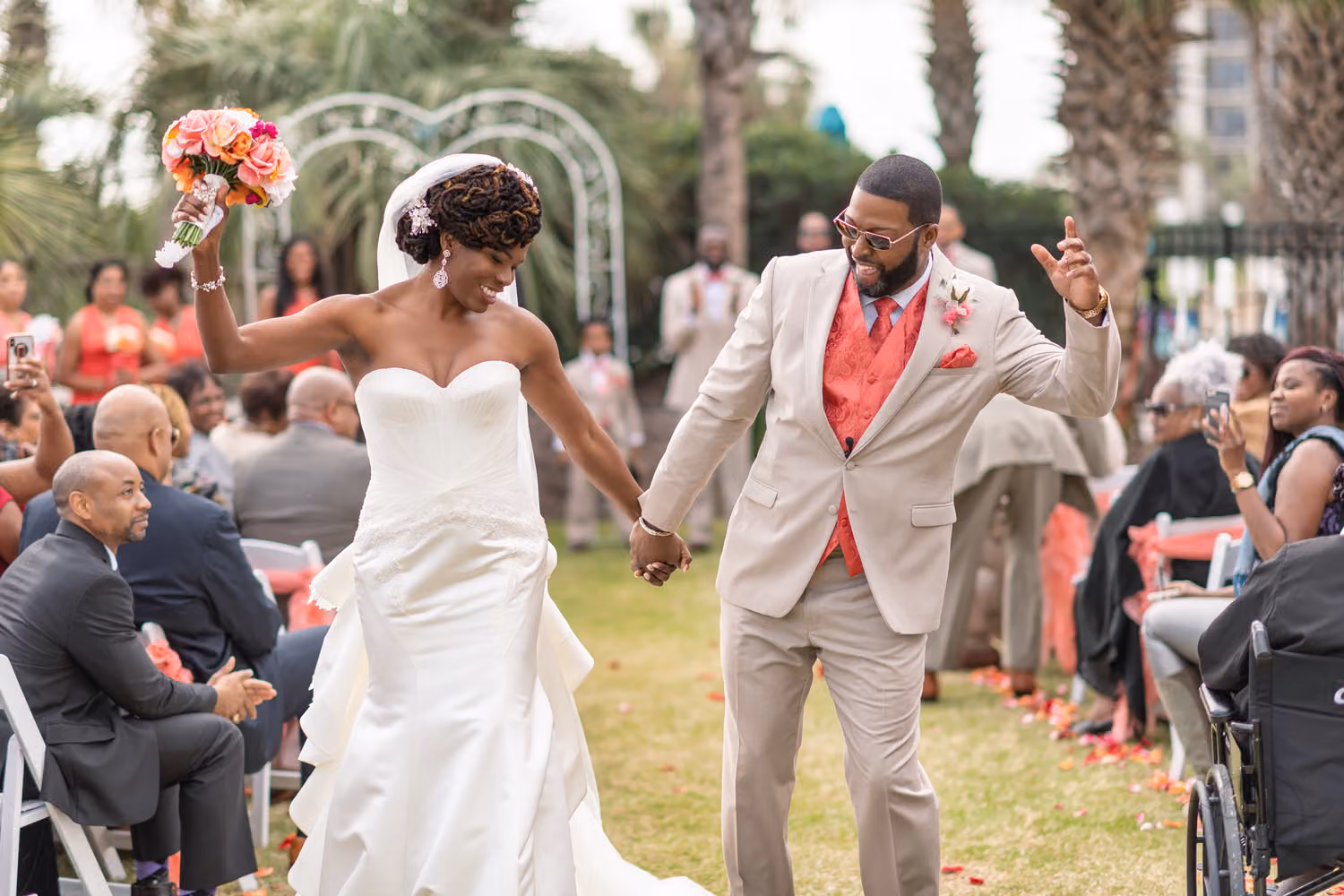 Bride raising her bouquet as she and the groom cheer walking up the aisle at the DoubleTree Resort in Myrtle Beach