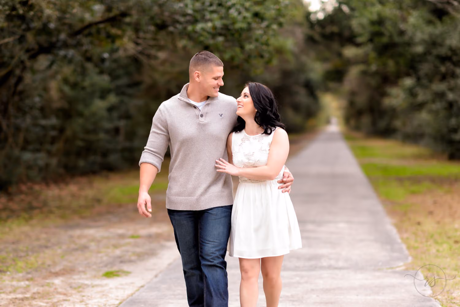 Engaged couple walking arm in arm down a long tree-lined path near Atalaya Castle at Huntington Beach State Park