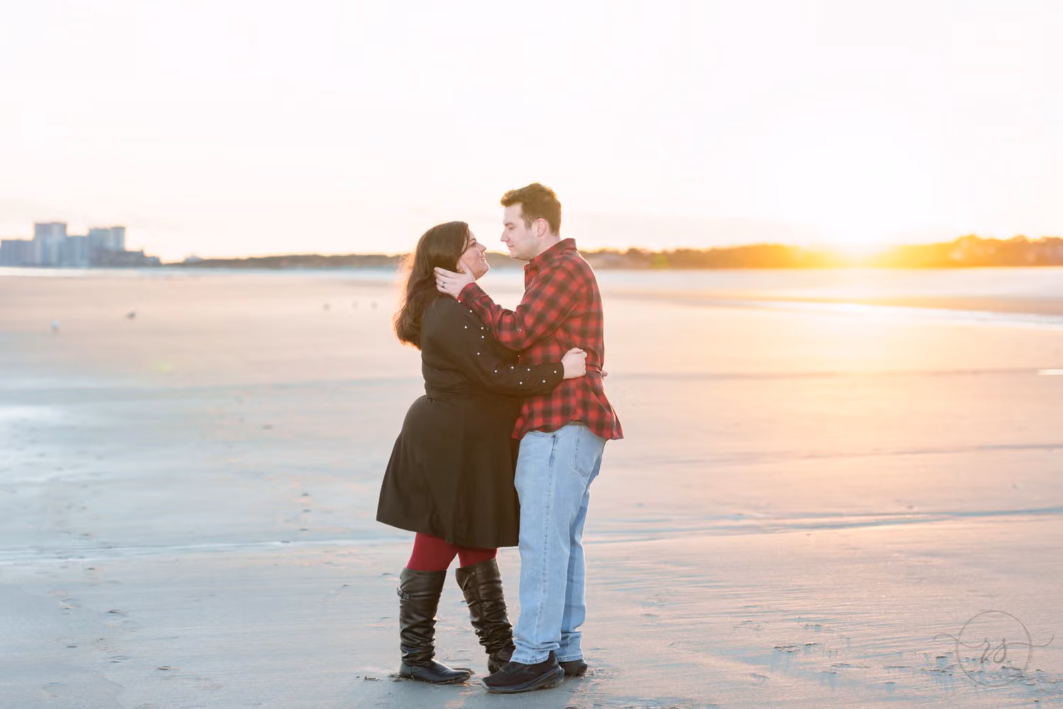 Couple in winter coats and boots kissing on the beach as the sun sets in North Myrtle Beach