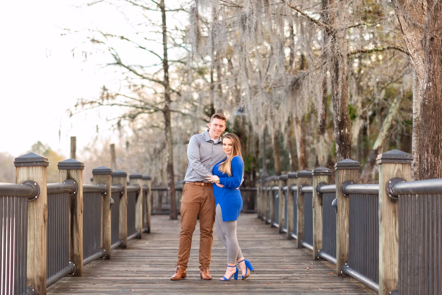 Couple standing close on a wooden boardwalk under bare trees draped in Spanish moss along the Conway Riverwalk