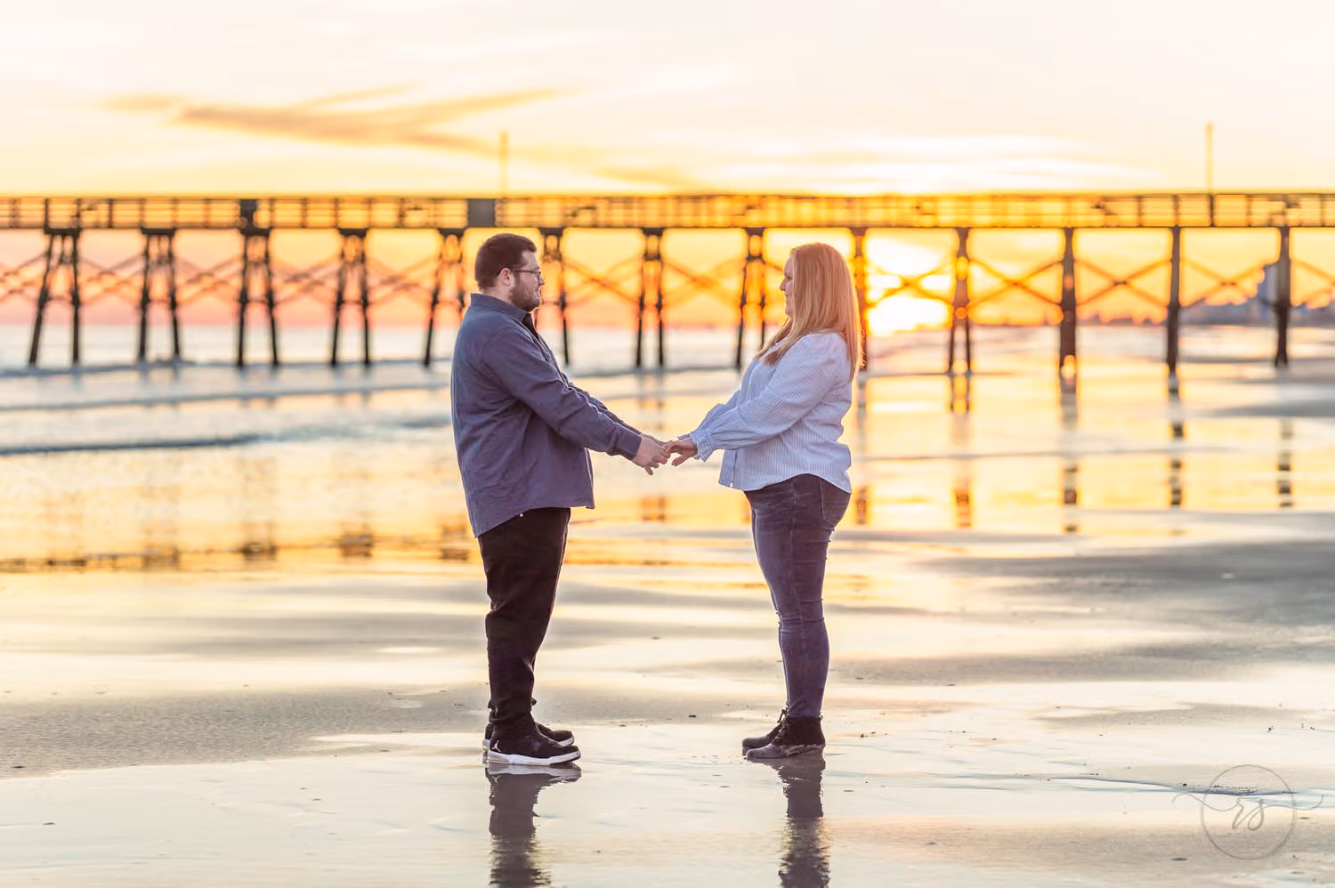 Couple holding hands on the wet sand as the winter sun sets behind the pier in North Myrtle Beach
