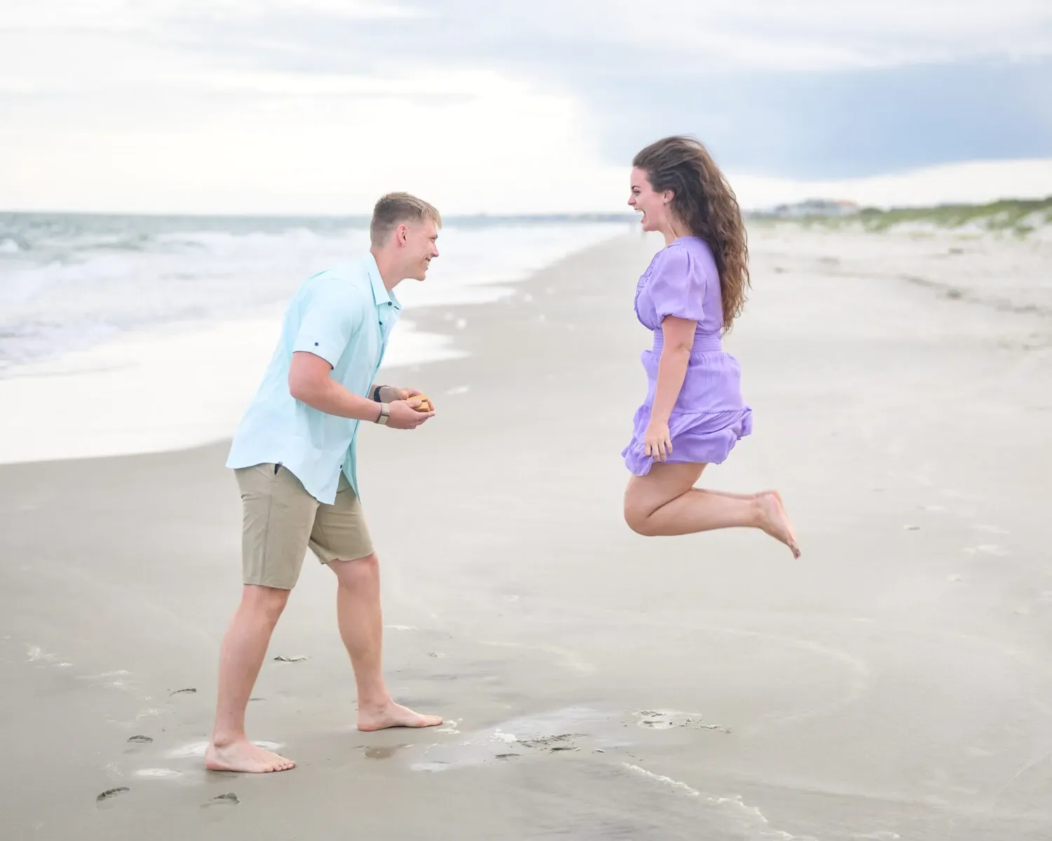 Woman leaping into the air on the beach as her partner proposes at Huntington Beach State Park