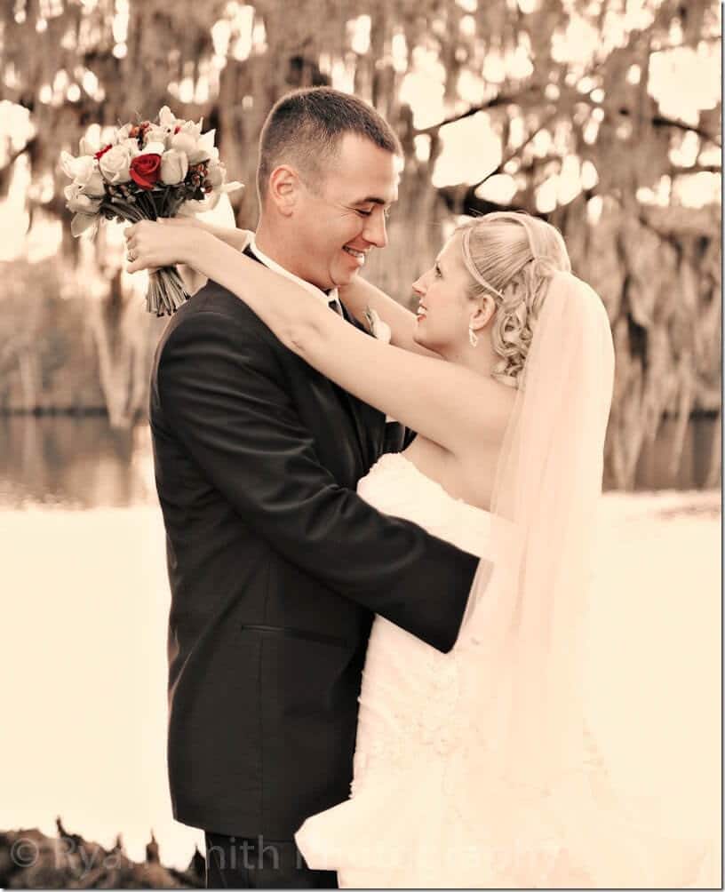 Bride and groom smiling at each other by water
