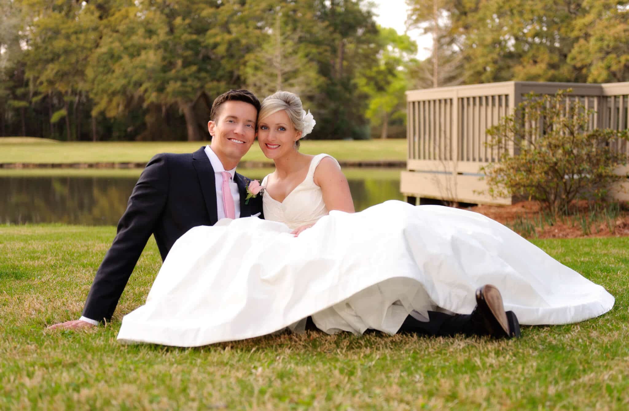 Bride and groom laying in grass in front of pond