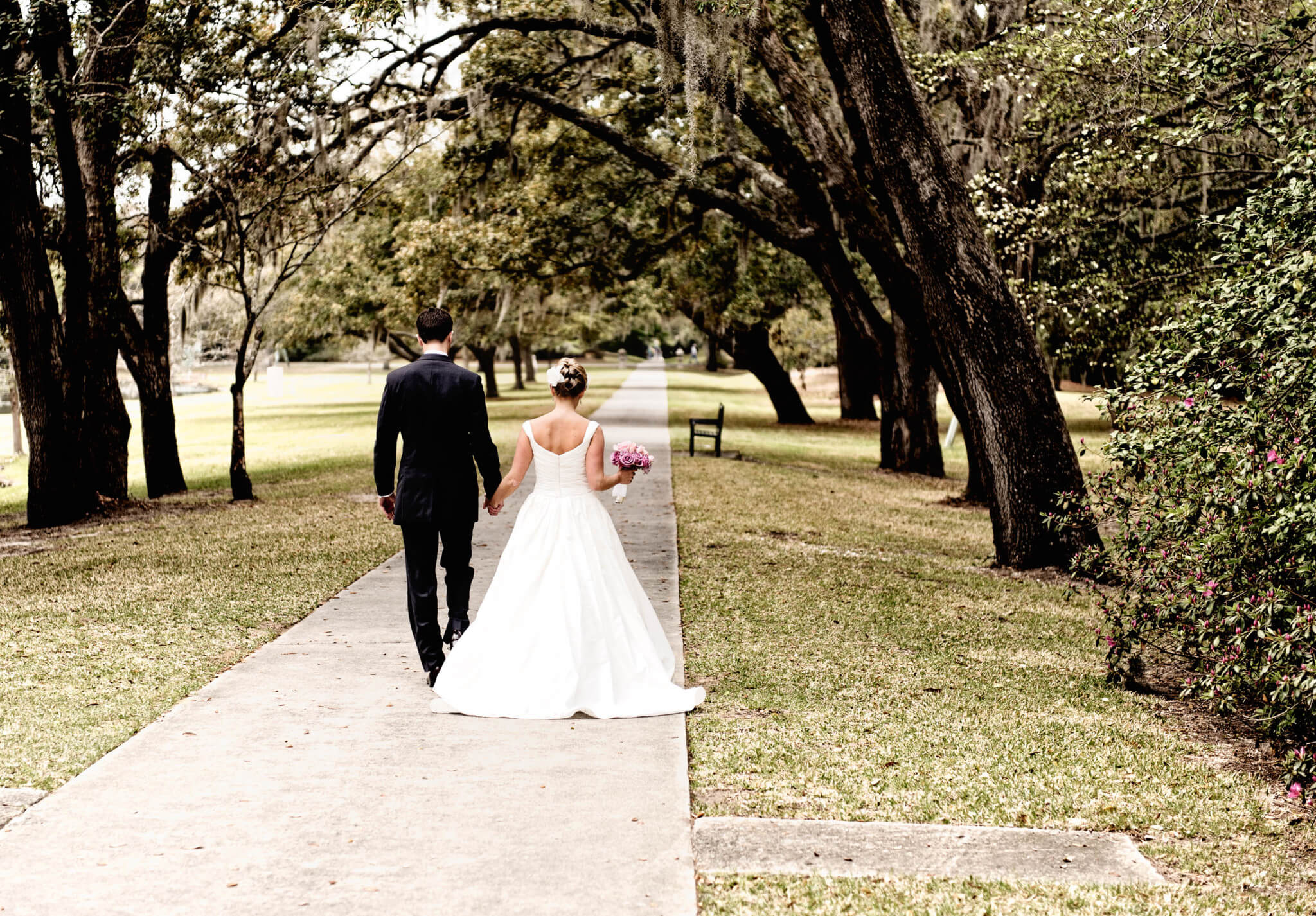 Bride and groom walking down sidewalk through the trees - modern