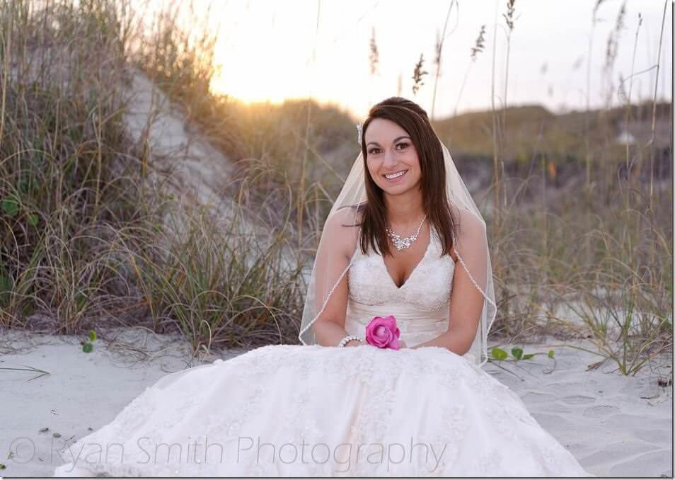 Bride sitting in front of sand dune backlit by sunset