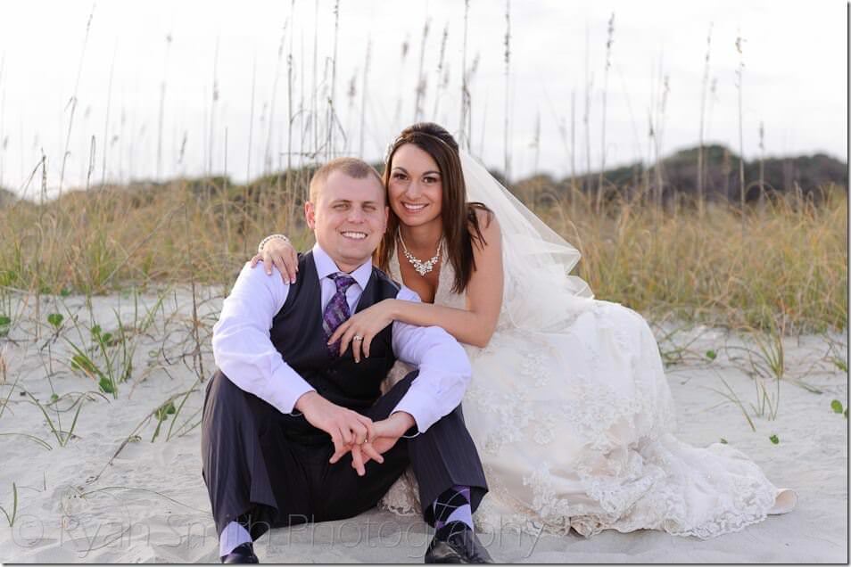 Bride leaning over behind groom in front of the sand dunes