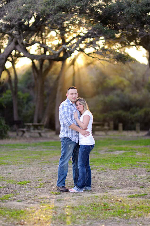Couple hugging in front streams of sunlight through the oak trees -