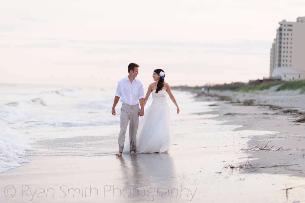 Bride and groom holding hands and walking in the edge of the ocean - Ocean Isle