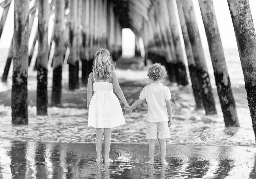 Brother and sister holding hands looking at the ocean