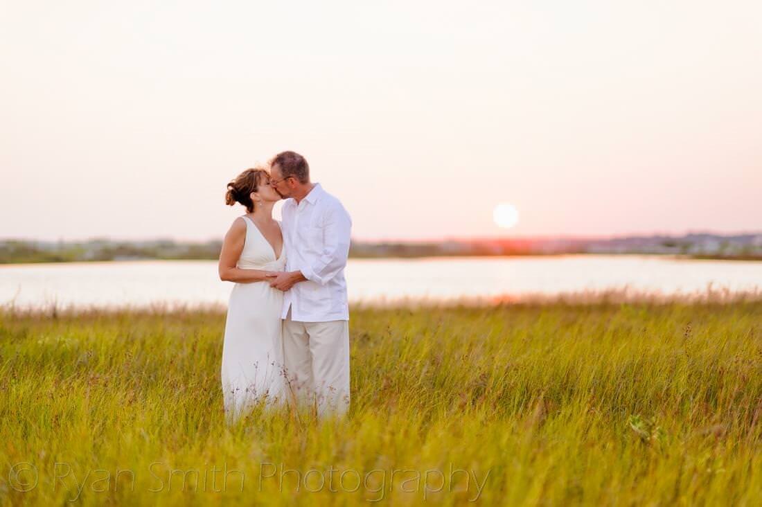 Bride and groom kissing in the tall grass by the late - Holden Beach, NC