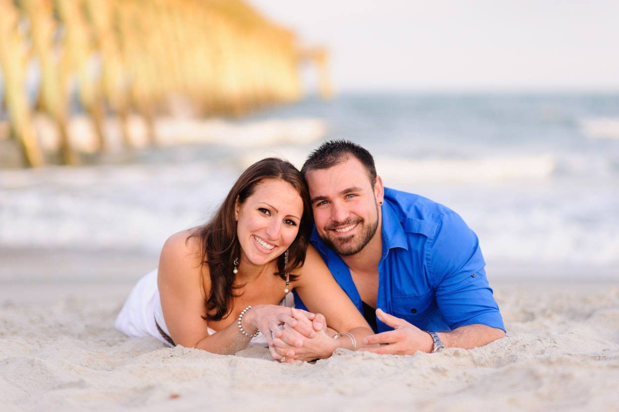 Engagement portrait laying in the sand together holding hands