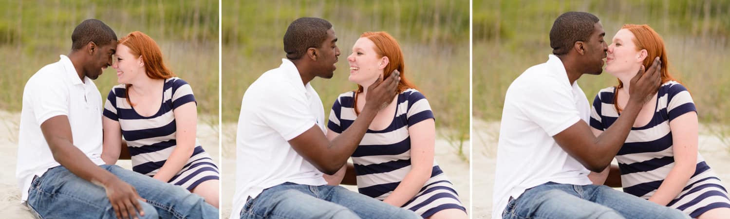 Couple sitting beside each other in the sand and kissing