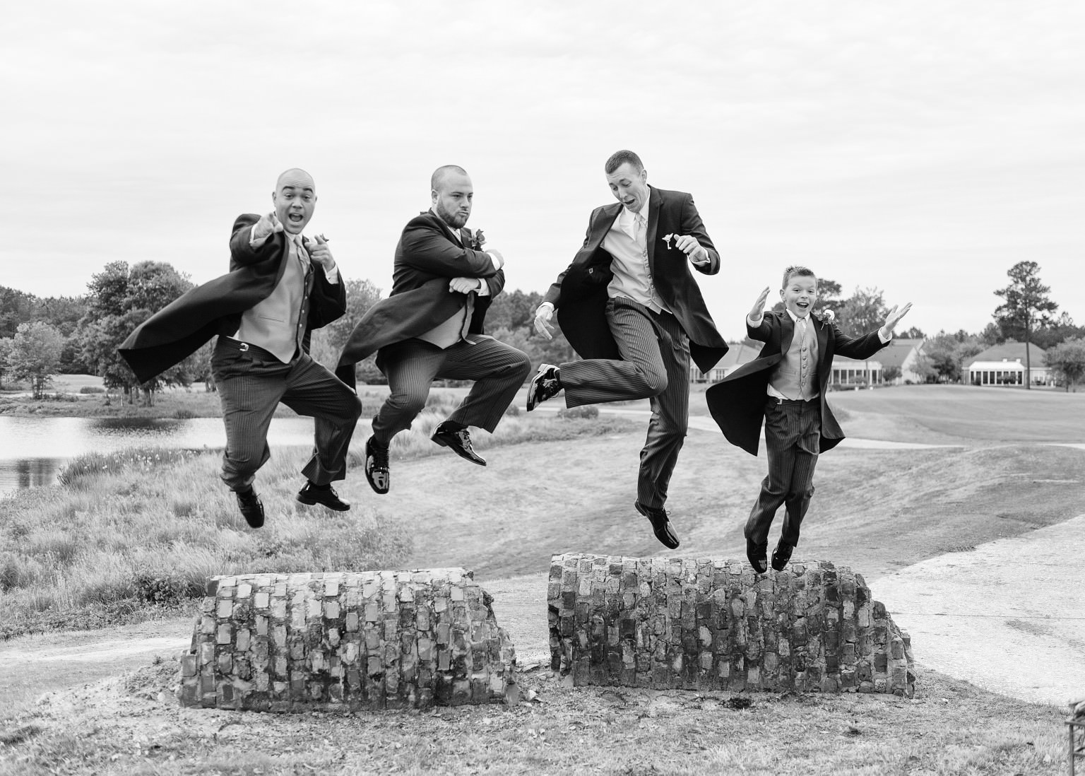 Groomsmen jumping off ruins in black and white