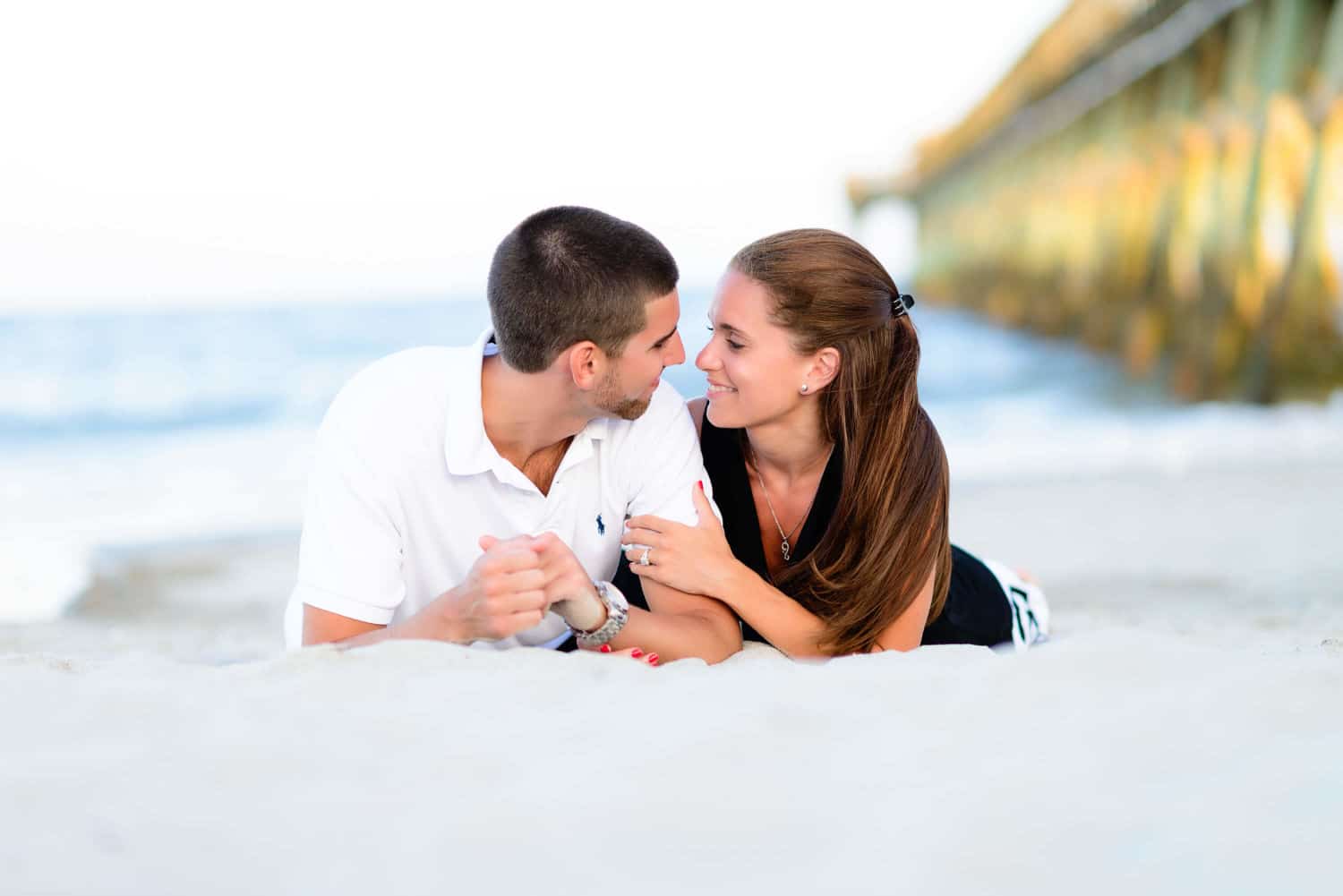 Couple laying in the sand smiling at each other in front of the ocean - Myrtle Beach State Park