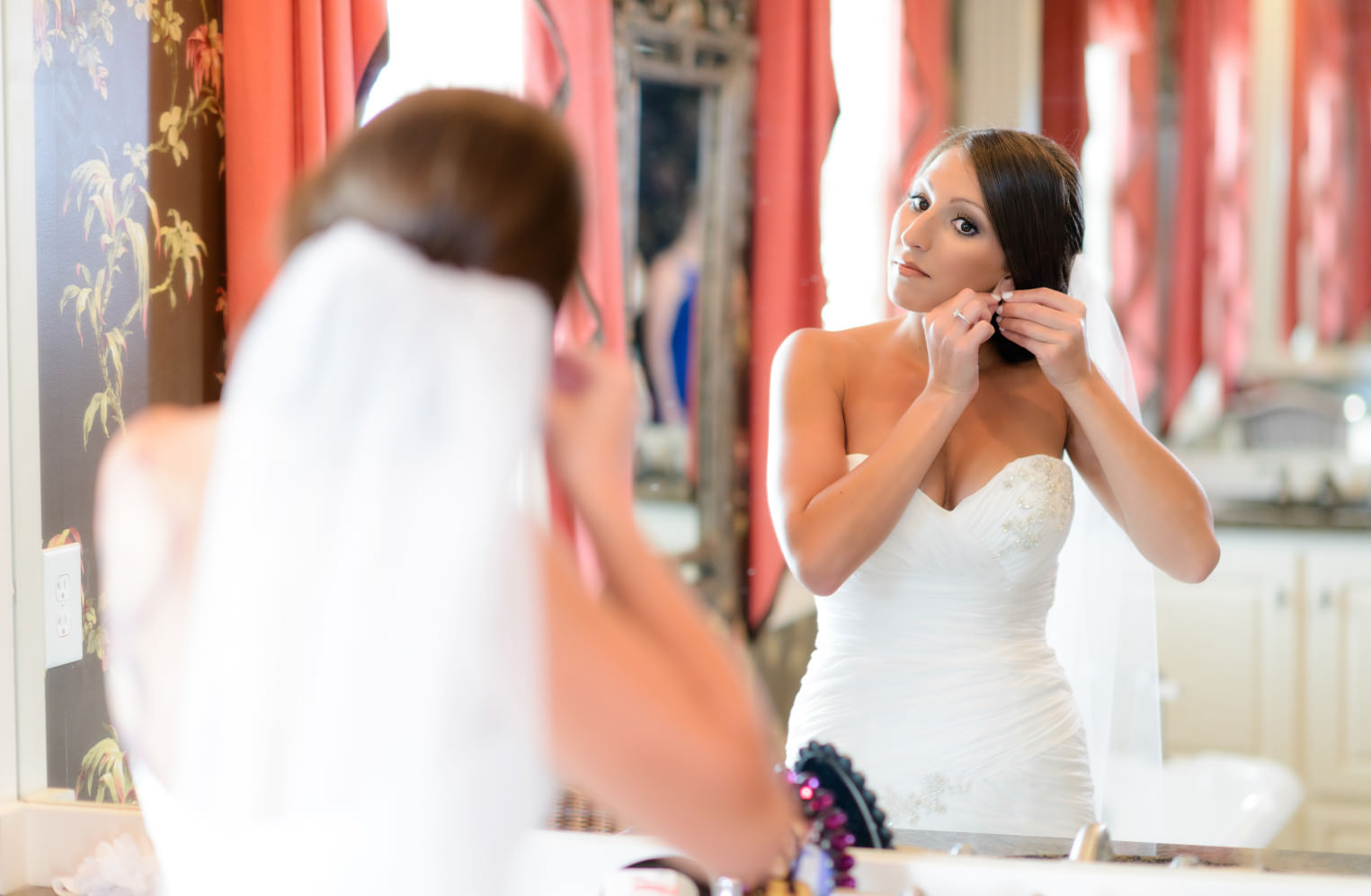 Bride putting on earrings in the mirror