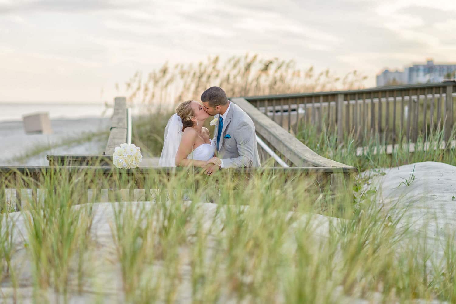 Portrait of bride and groom kissing behind the sea grass at the Ocean Club in Myrtle Beach