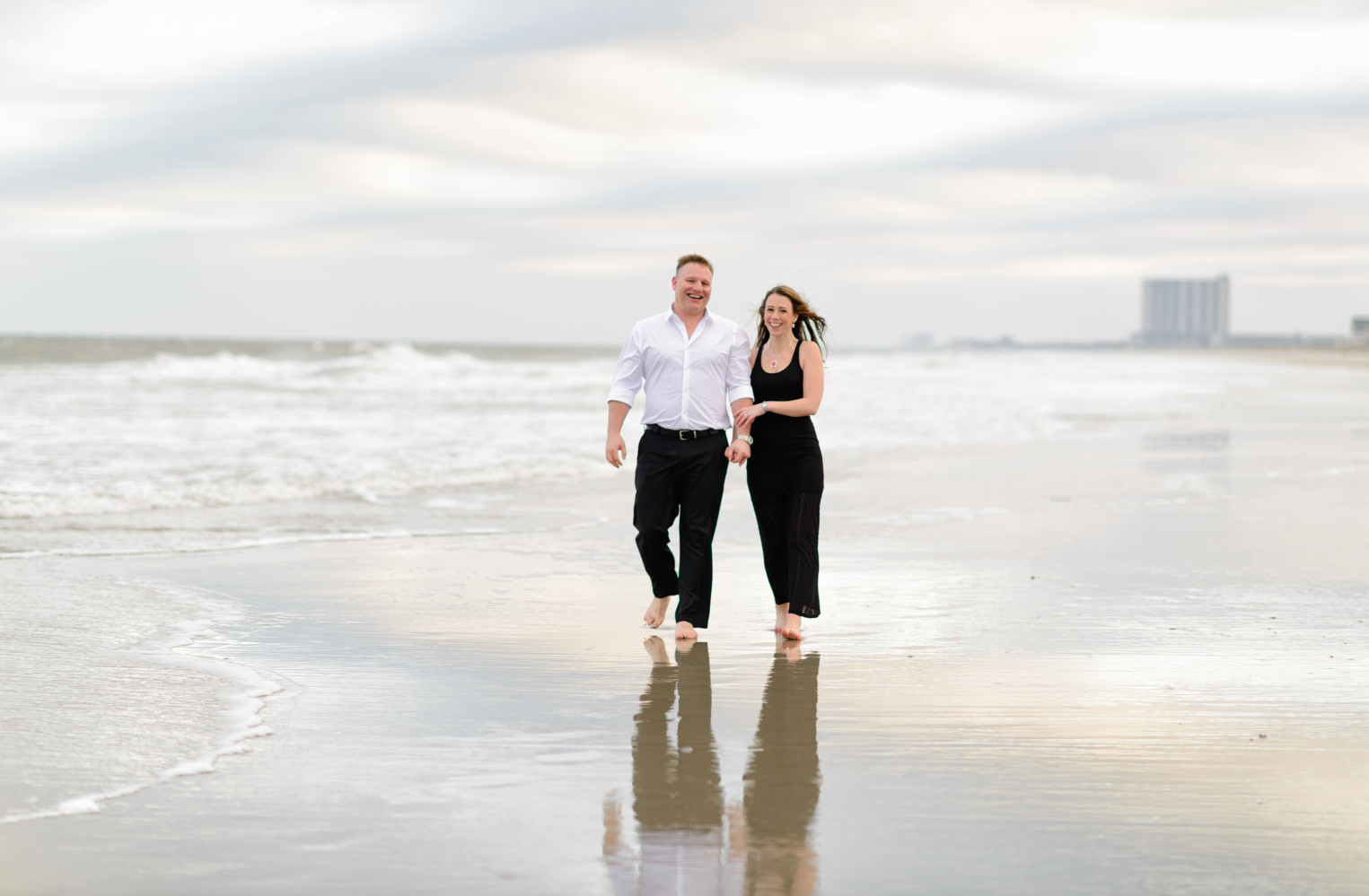 Engagement portrait couple walking down the beach with a reflection of the sky in the water