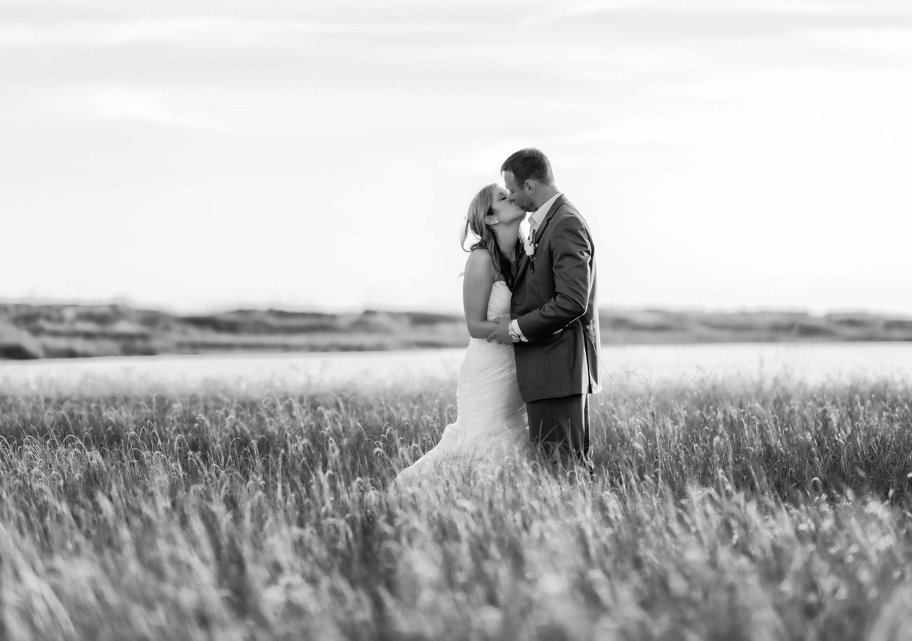 Black and white of couple kissing with sunlight reflecting on the beach grass - Holden Beach