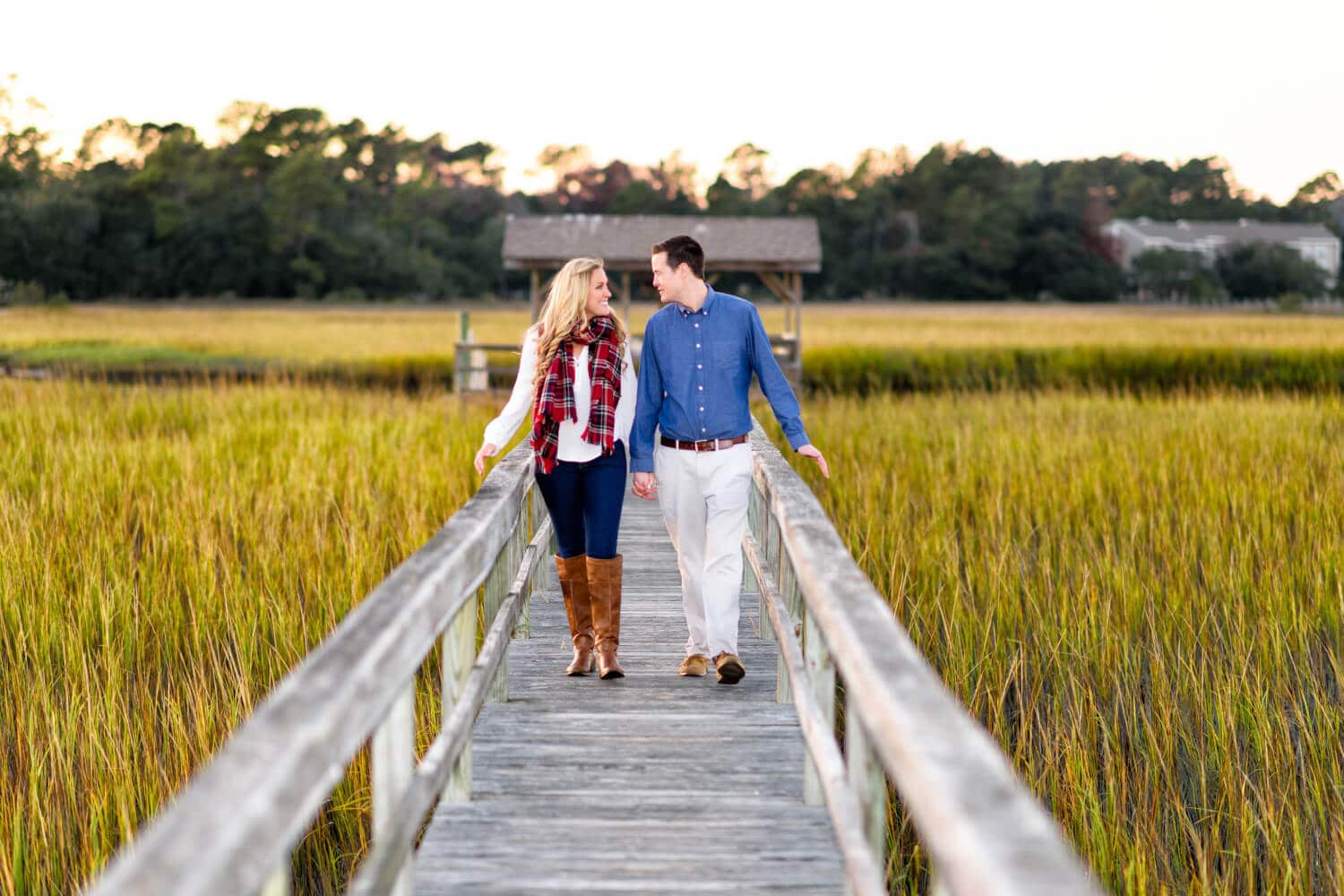 Couple walking down marsh boardwalk together at sunset