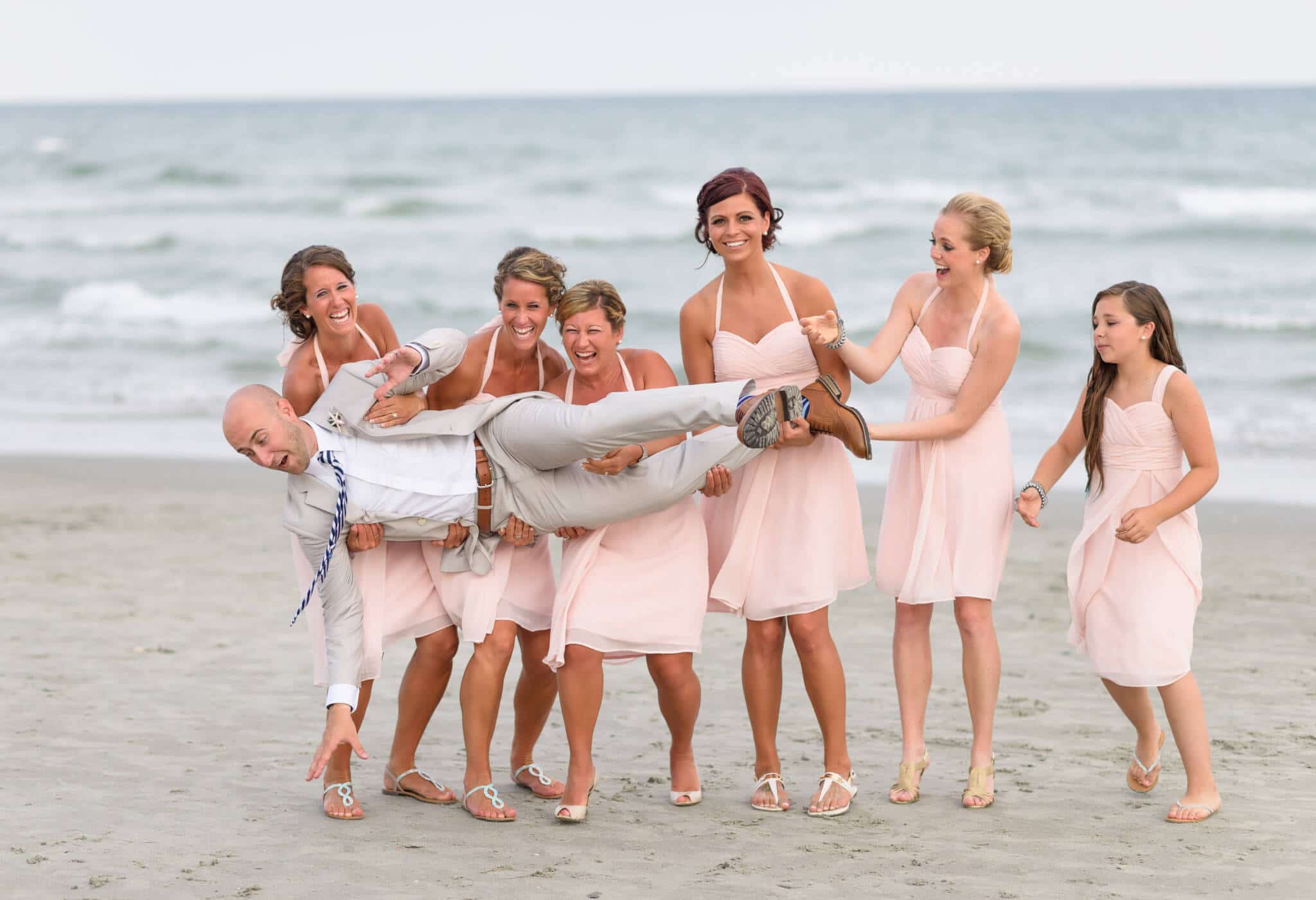 Bridesmaids dropping the groom on the beach