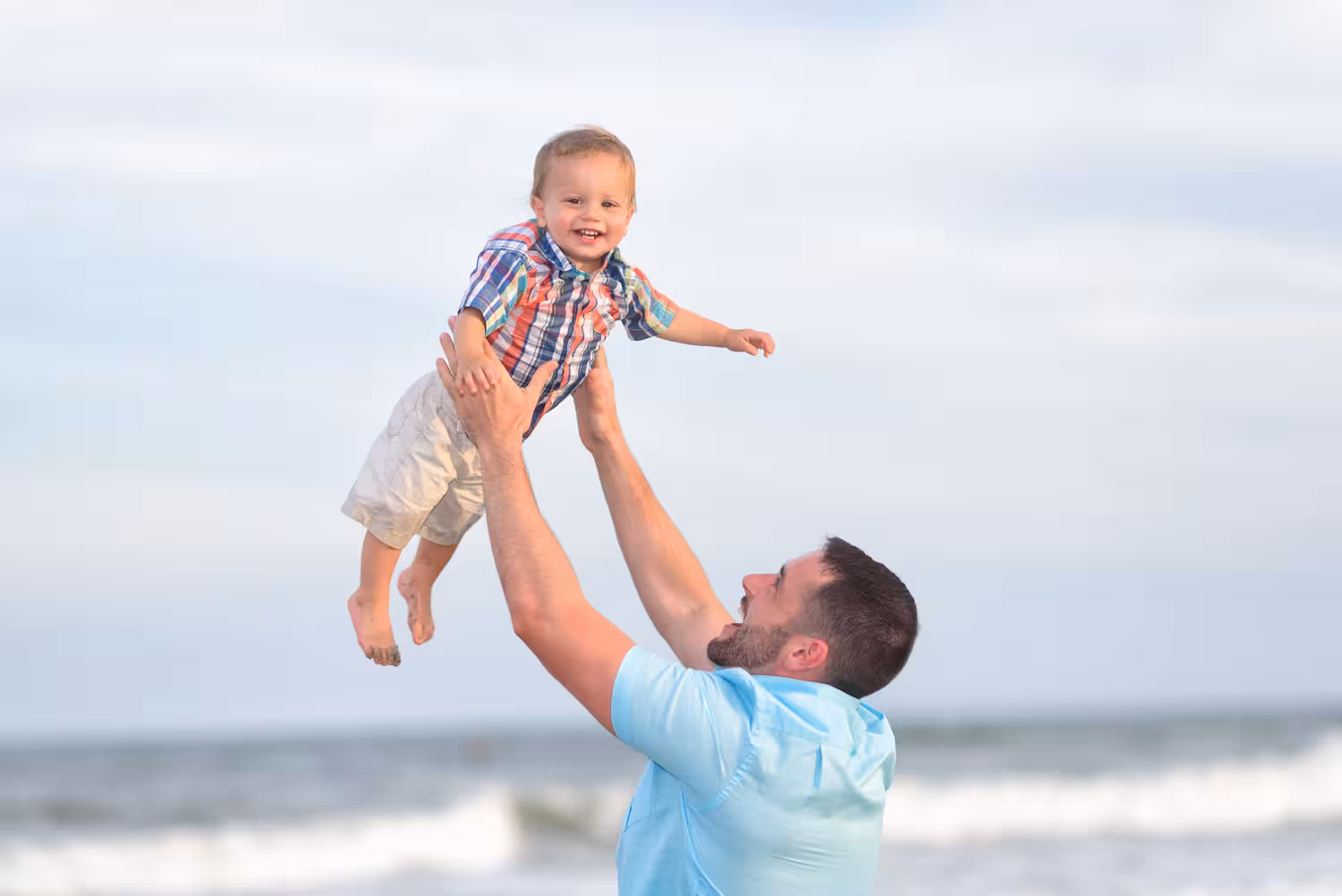 Little boy being held in the air in front of the ocean - 85mm f1.4 lens