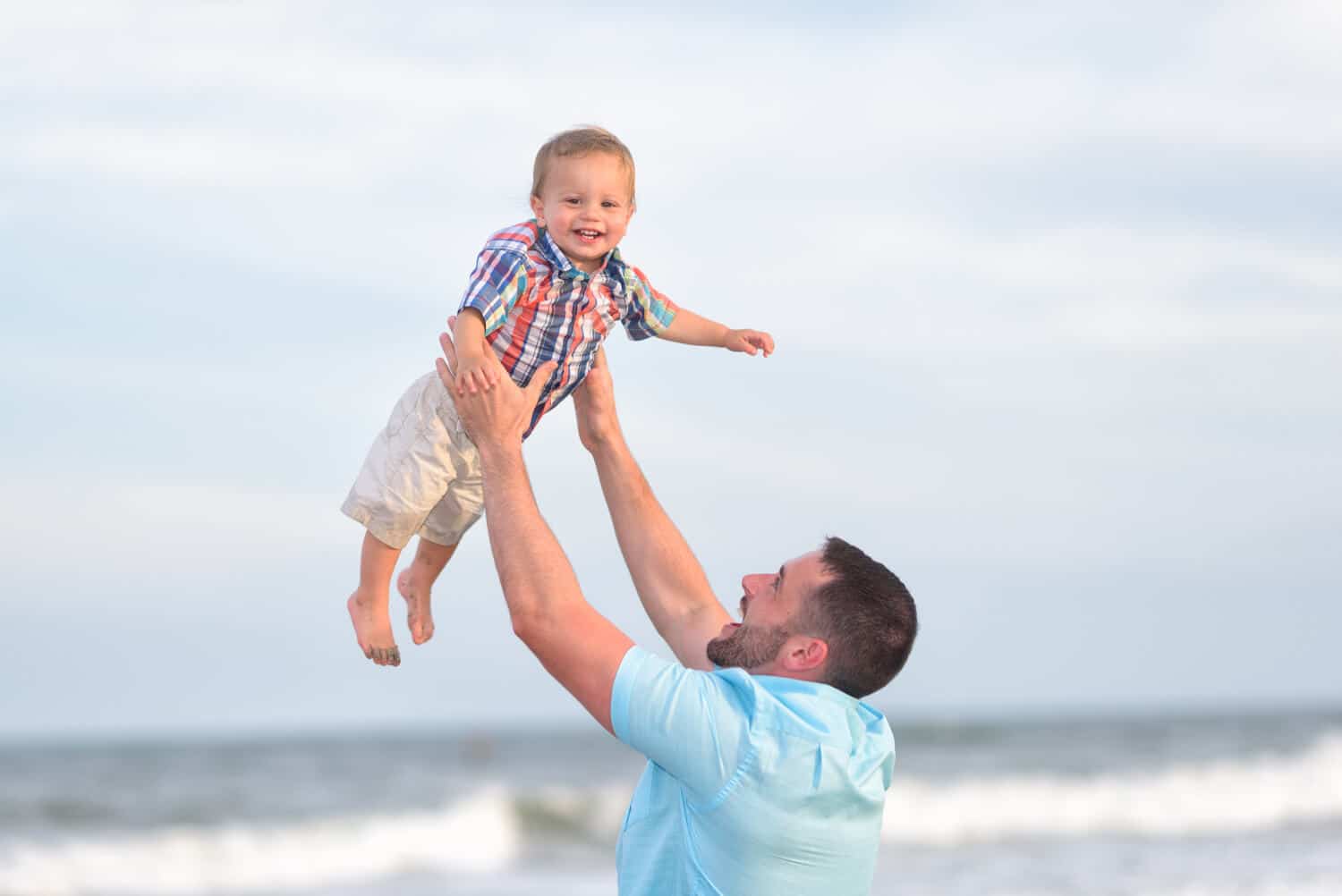 Little boy being held in the air in front of the ocean - 85mm f1.4 lens