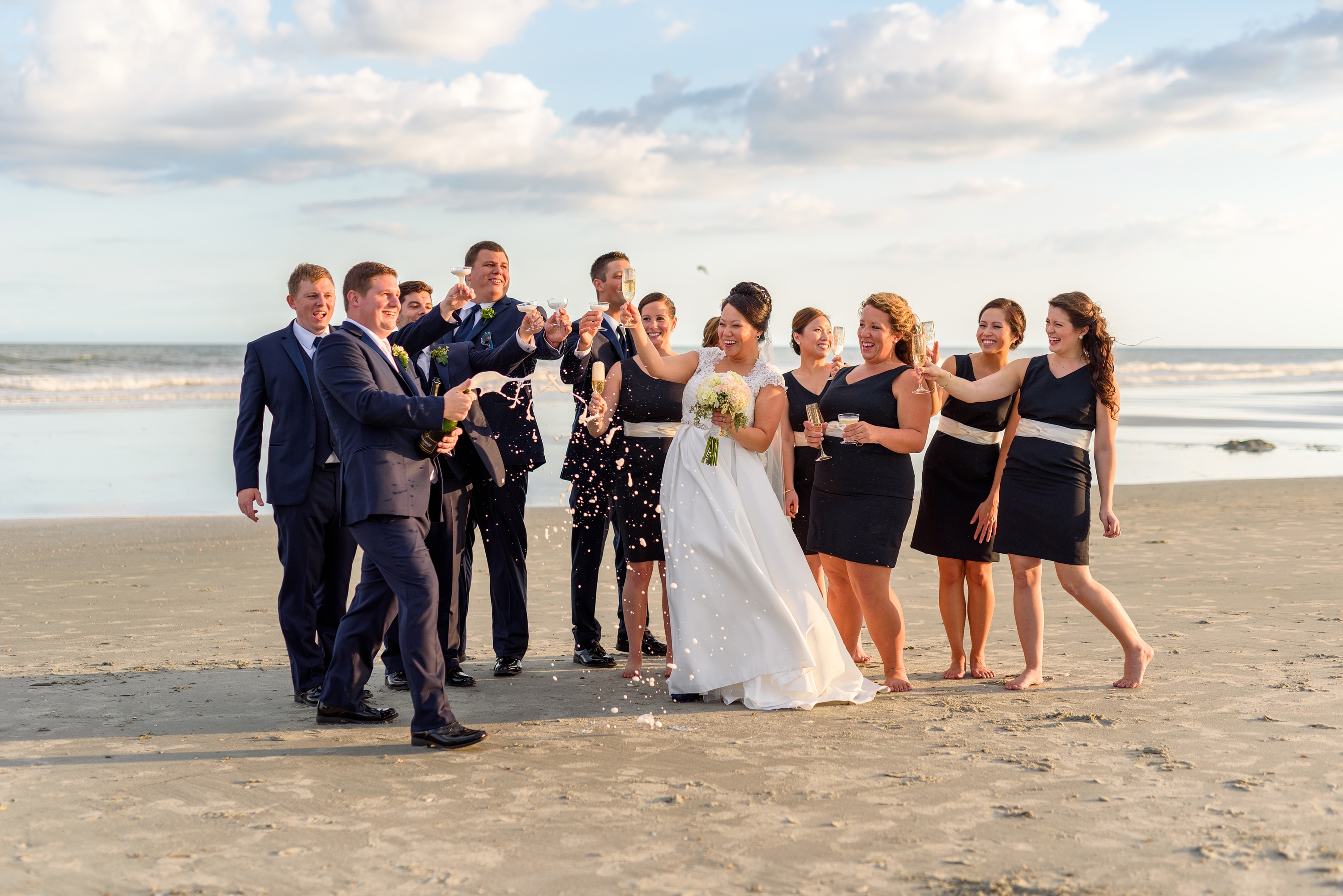 Bridal party opening a champagne bottle together on the beach