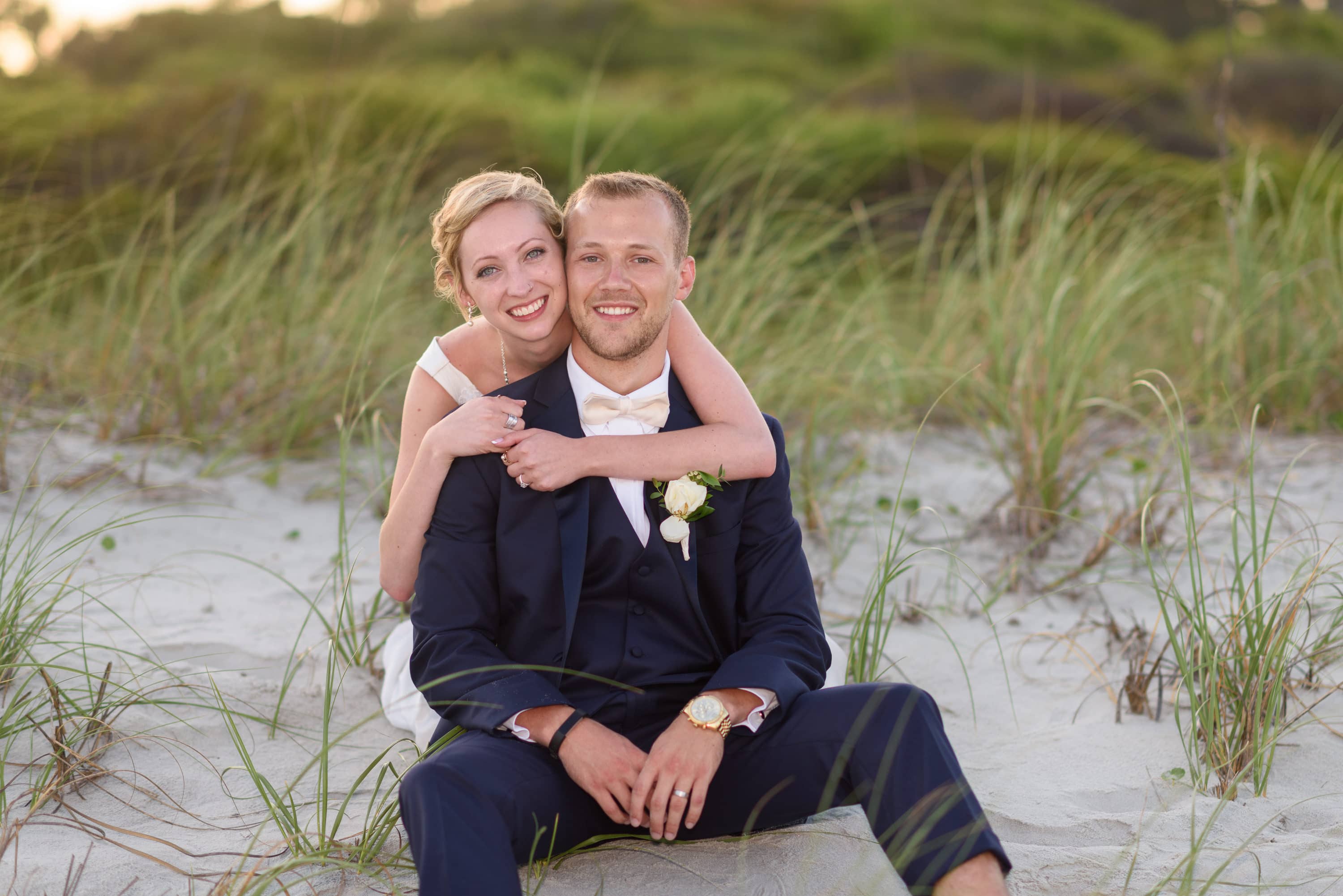 Bride with her arms around groom sitting on beach -  Grande Dunes Ocean Club
