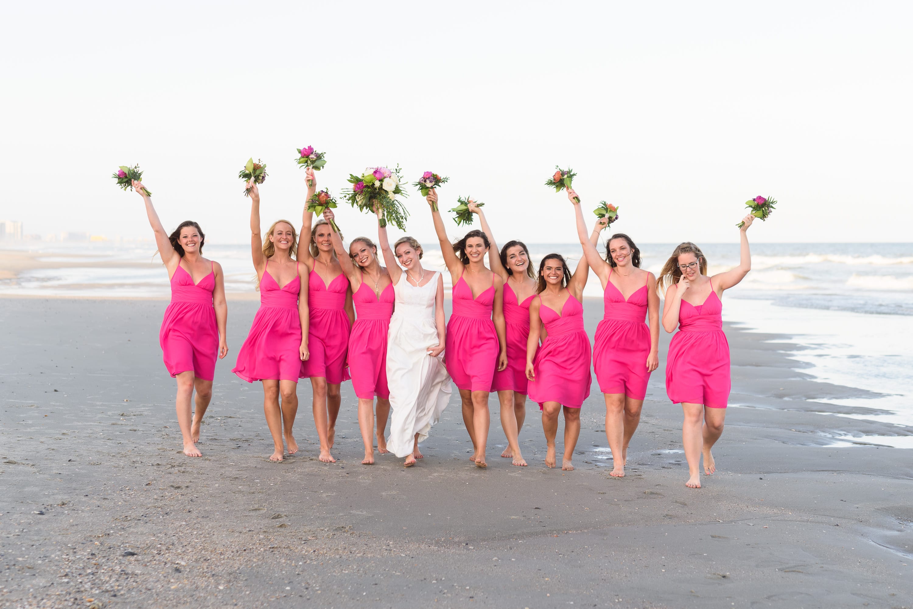 Girls walking down the beach holding up the flowers -  Grande Dunes Ocean Club