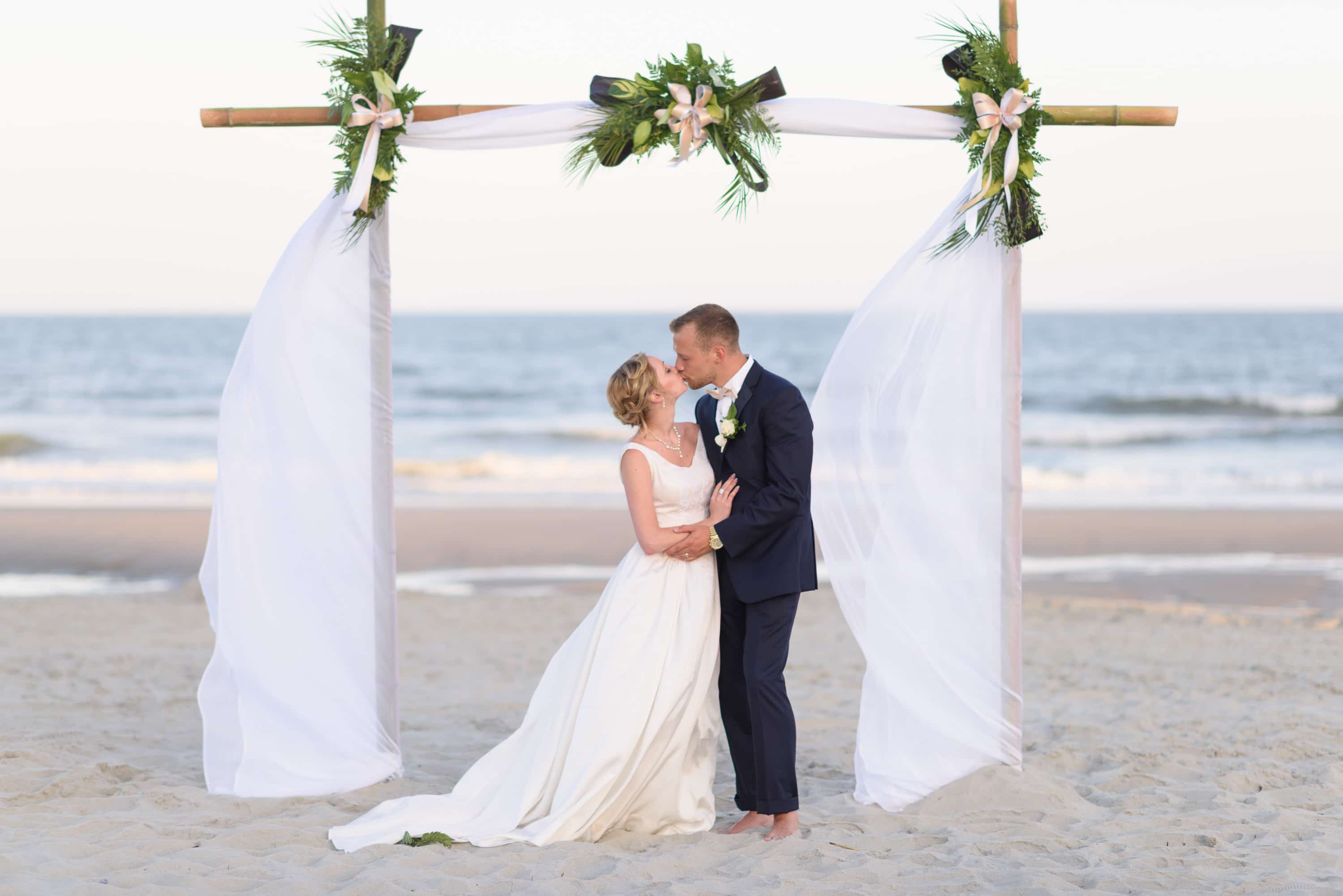 Kiss in front of the beach wedding arbor -  Grande Dunes Ocean Club