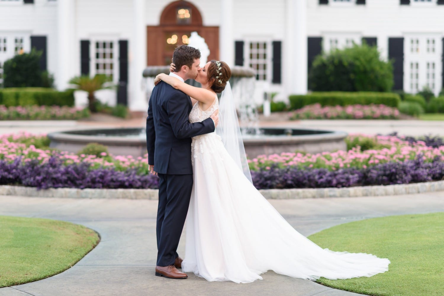 Bride kissing groom in front of the fountain and flowers Pine Lakes Country Club