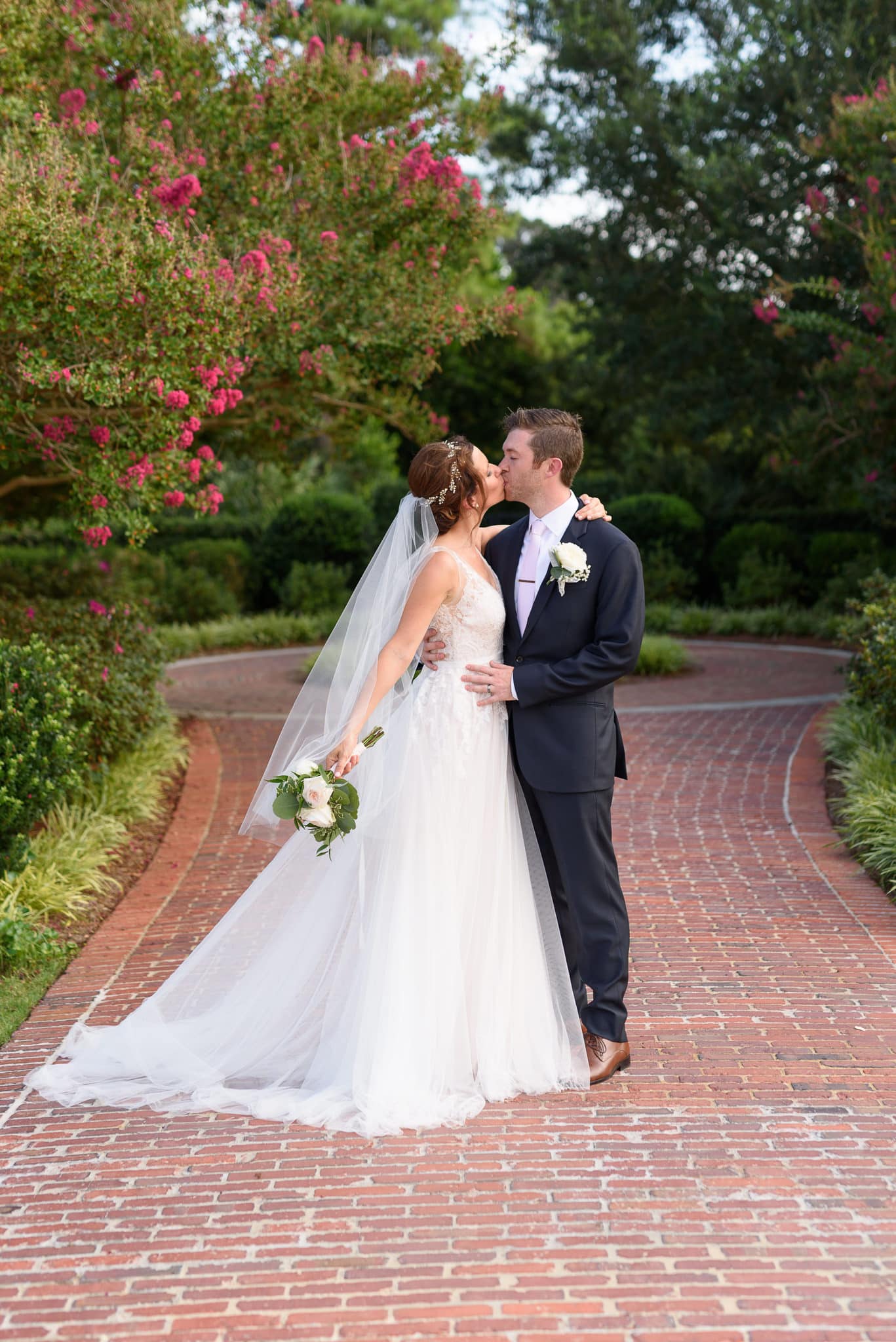Bride kissing groom on garden walkway Pine Lakes Country Club