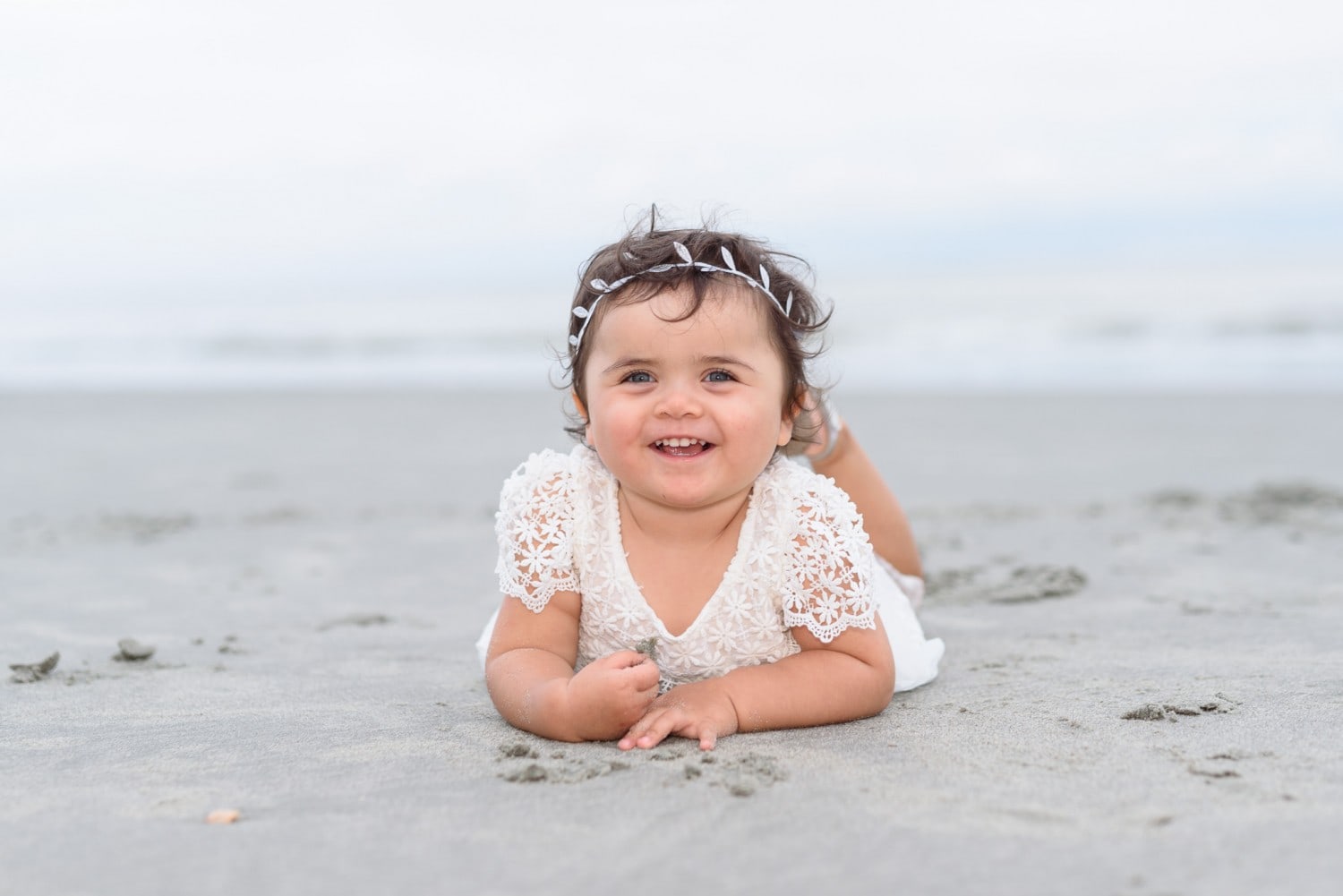Baby girl laying in the sand with a big smile - North Beach Plantation