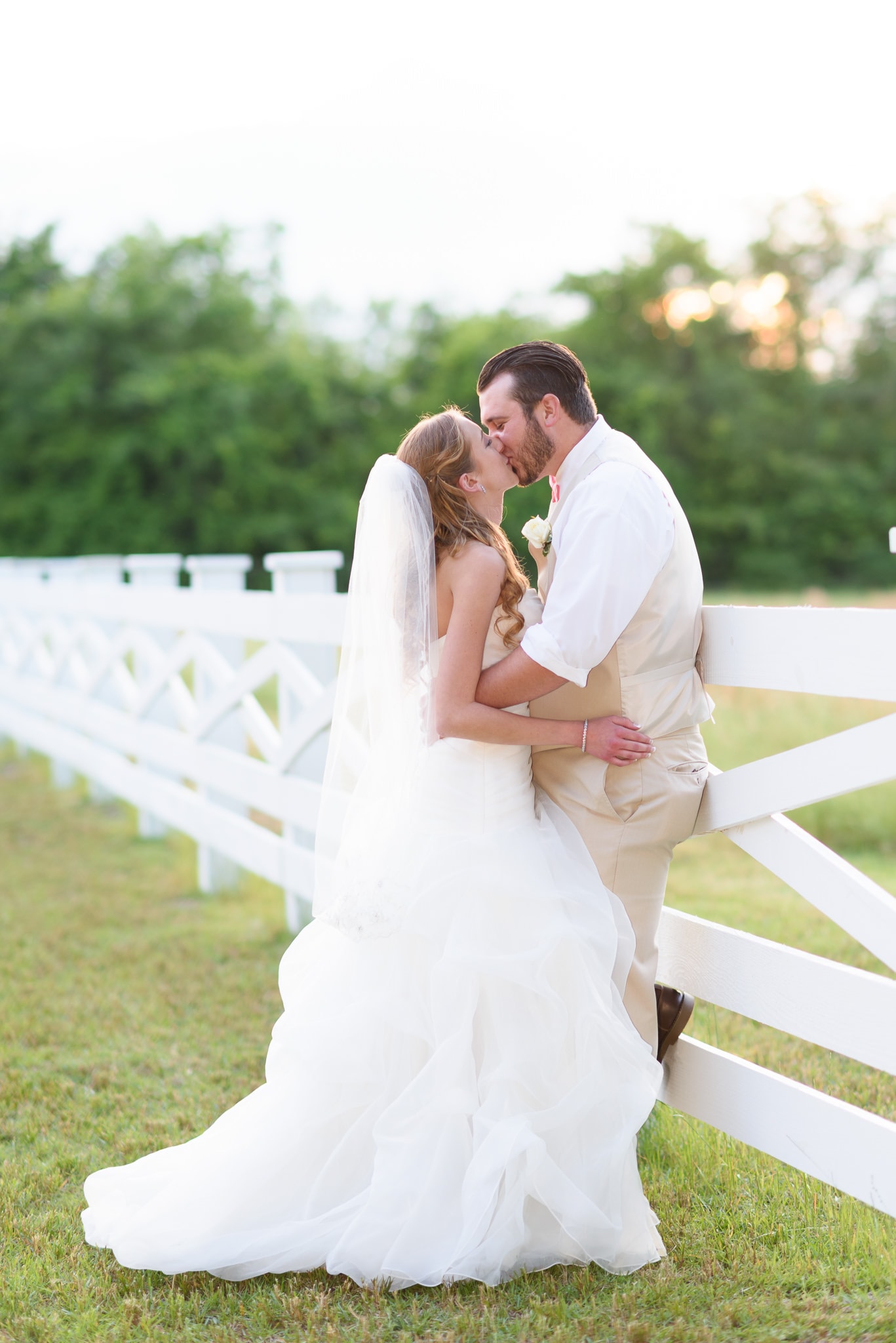 Bride and groom kissing against a white fence - Wildberry Farm