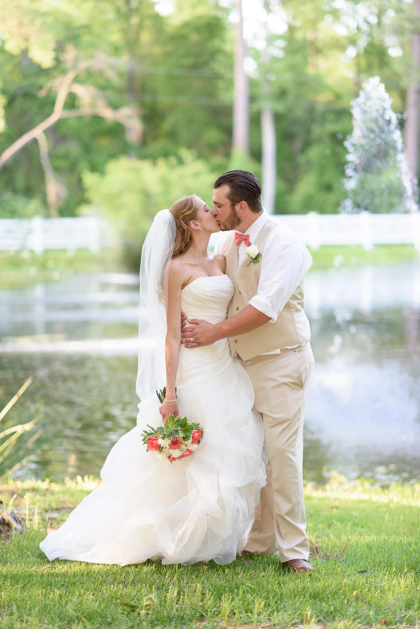 Bride and groom kissing in front of lake - Wildberry Farm