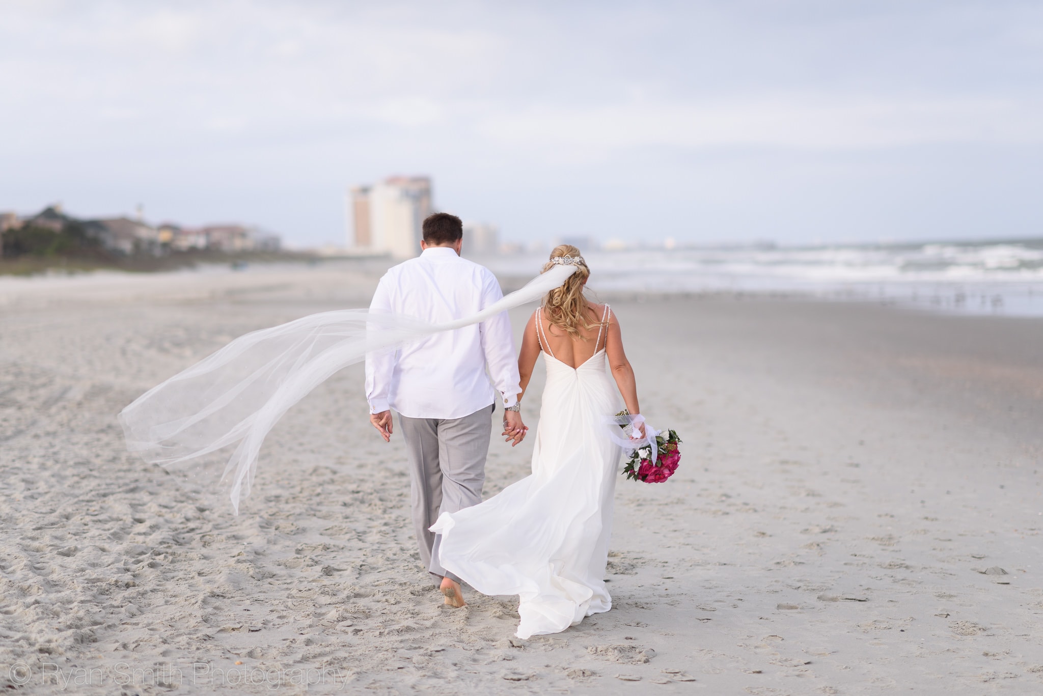 Bride and groom walking down the beach with long veil - Grande Dunes Ocean Club