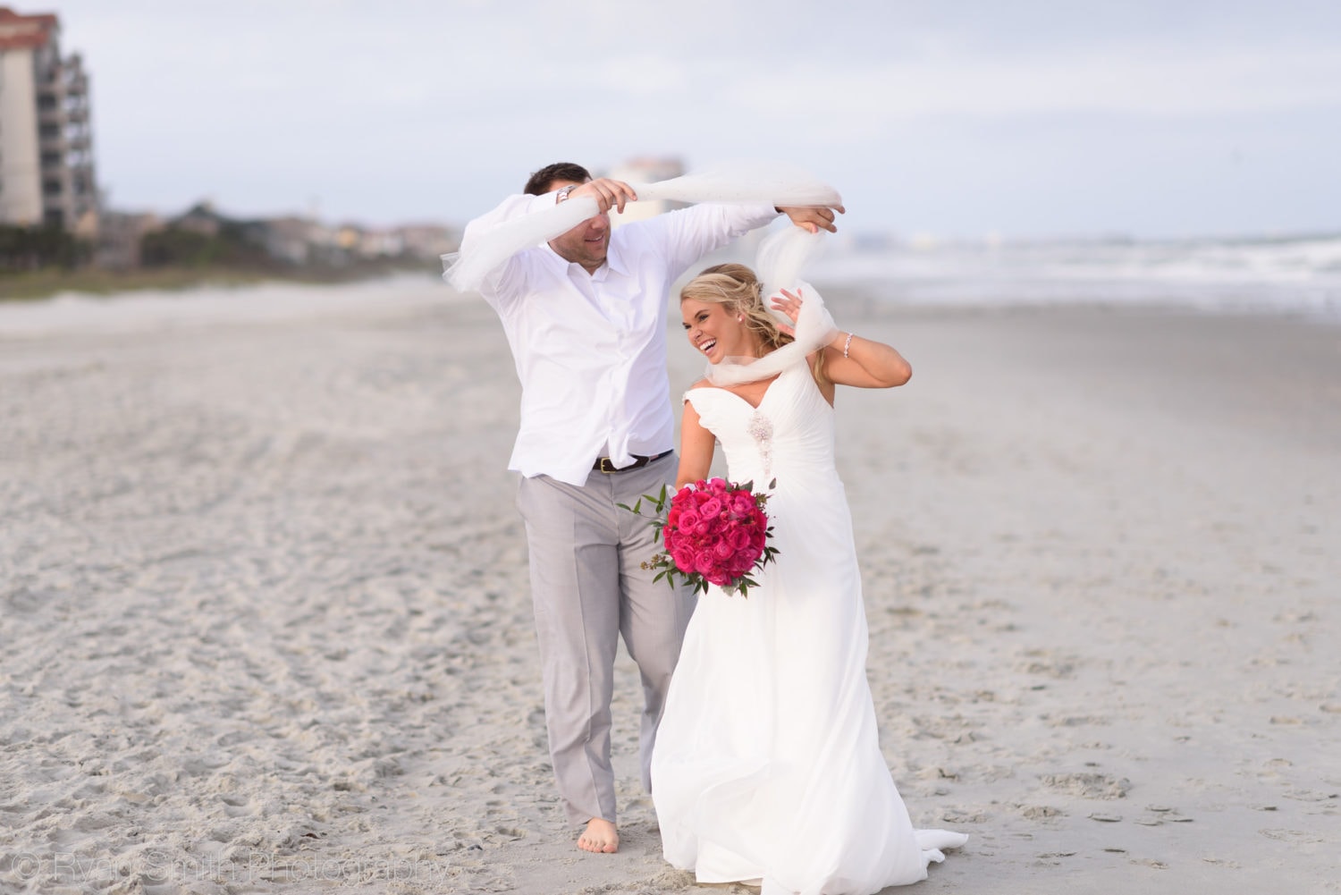 Bride and groom walking down the beach with long veil - Grande Dunes Ocean Club