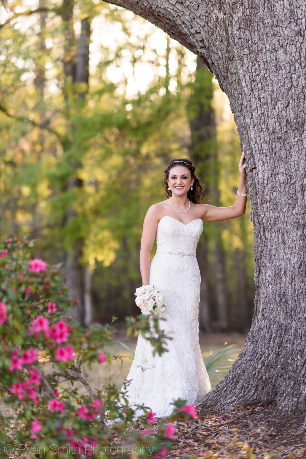 Bride leaning against a tree with flowers in the foreground  - Upper Mill Plantation