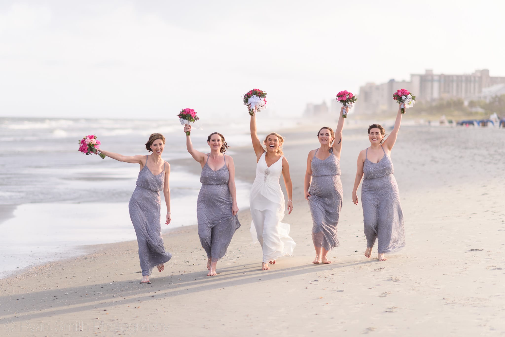Bridesmaids walking down beach holding flowers in the air - Grande Dunes Ocean Club
