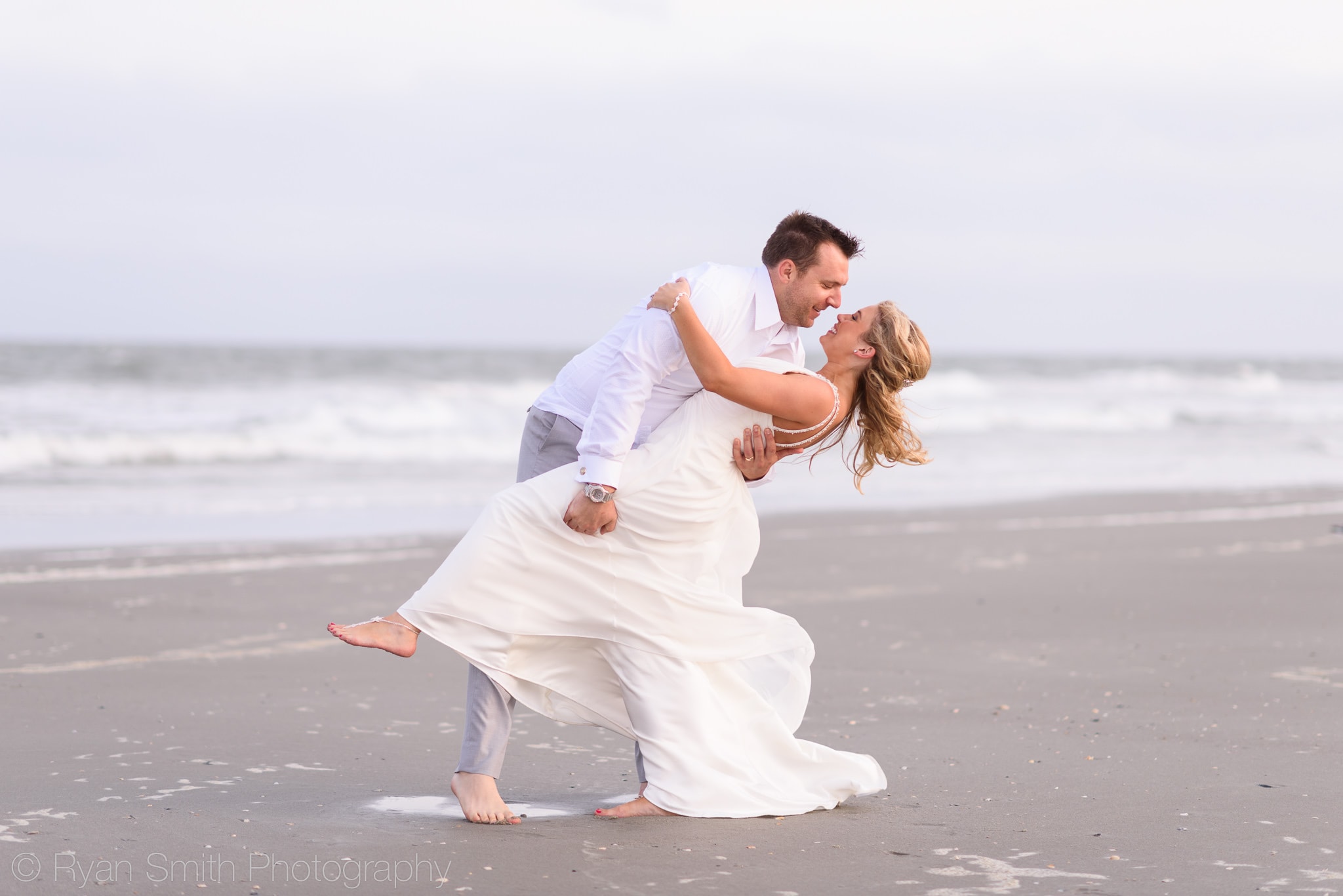 Groom dipping bride for a kiss by ocean - Grande Dunes Ocean Club