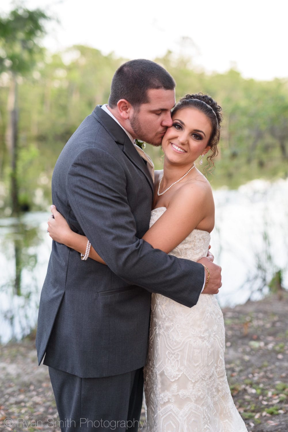 Groom kissing bride on the cheek by the river - Upper Mill Plantation