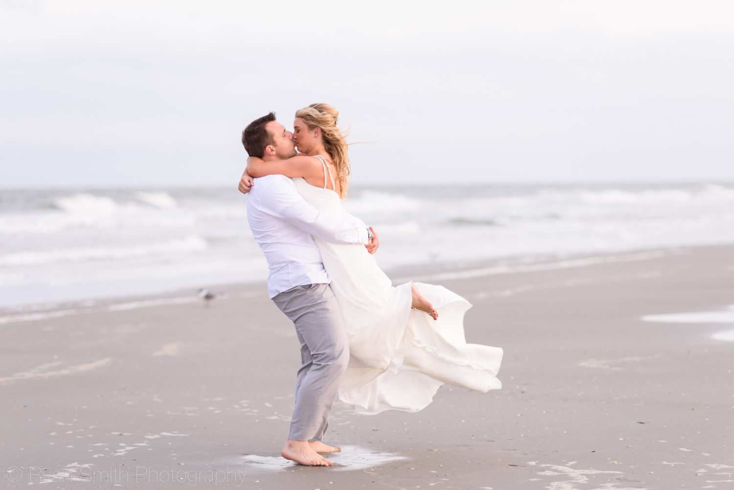 Groom lifting bride into the air for a kiss by ocean - Grande Dunes Ocean Club