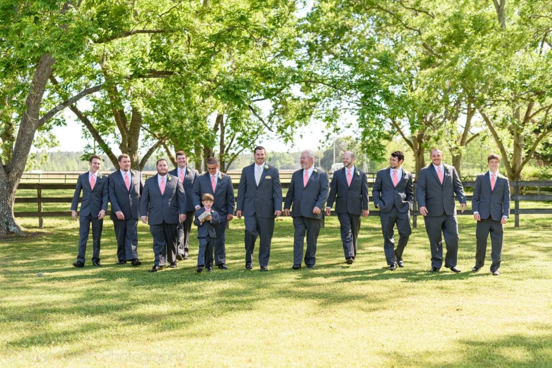 Groomsmen in gray suits walk across the lawn under the oak trees at Upper Mill Plantation